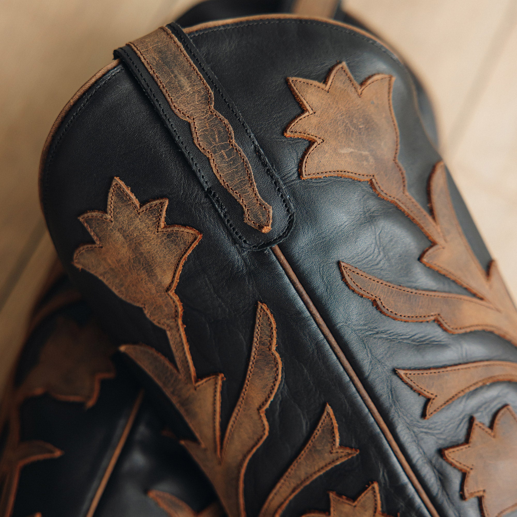 Close-up of black cowboy boots with intricate brown floral inlay designs and decorative stitching