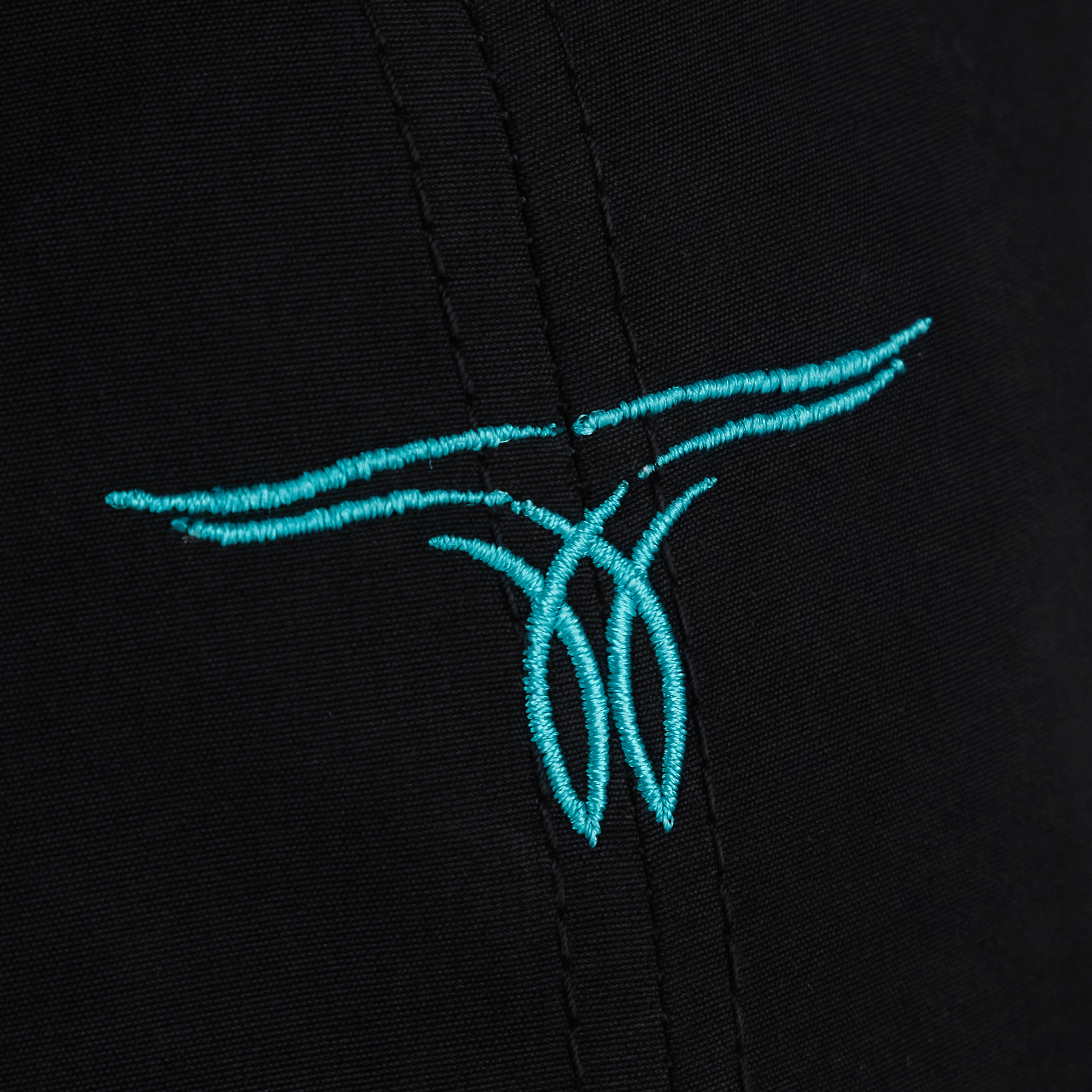 A close-up of a black hat with a turquoise embroidered logo