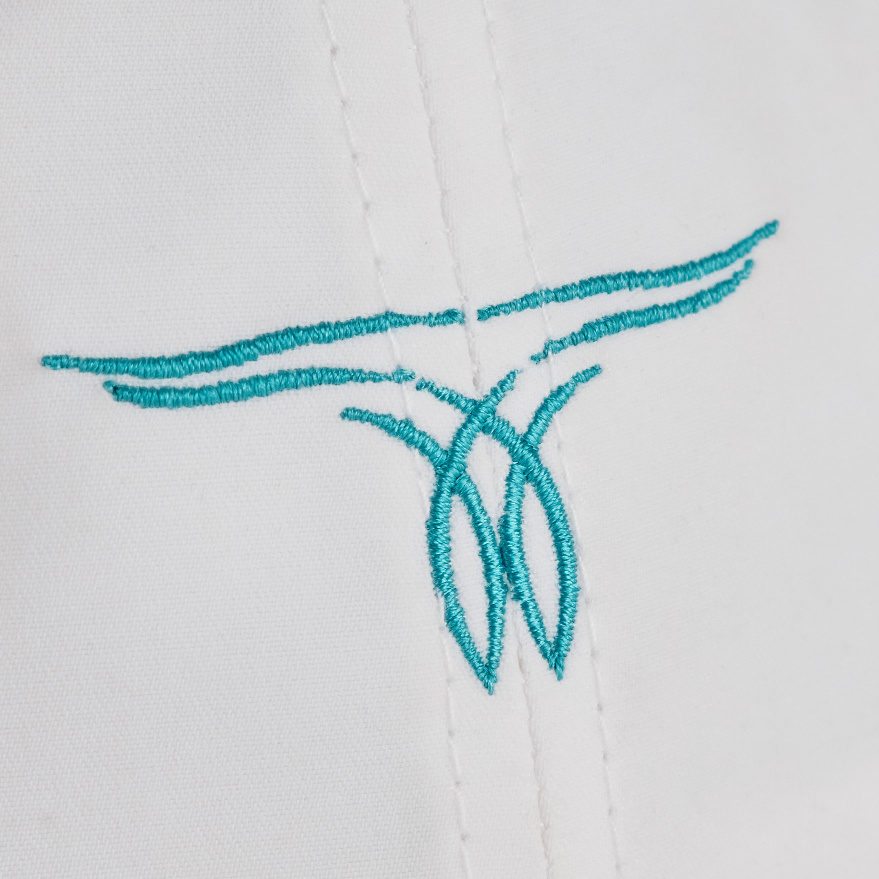 Close-up of a white Cinch hat with a turquoise embroidered logo