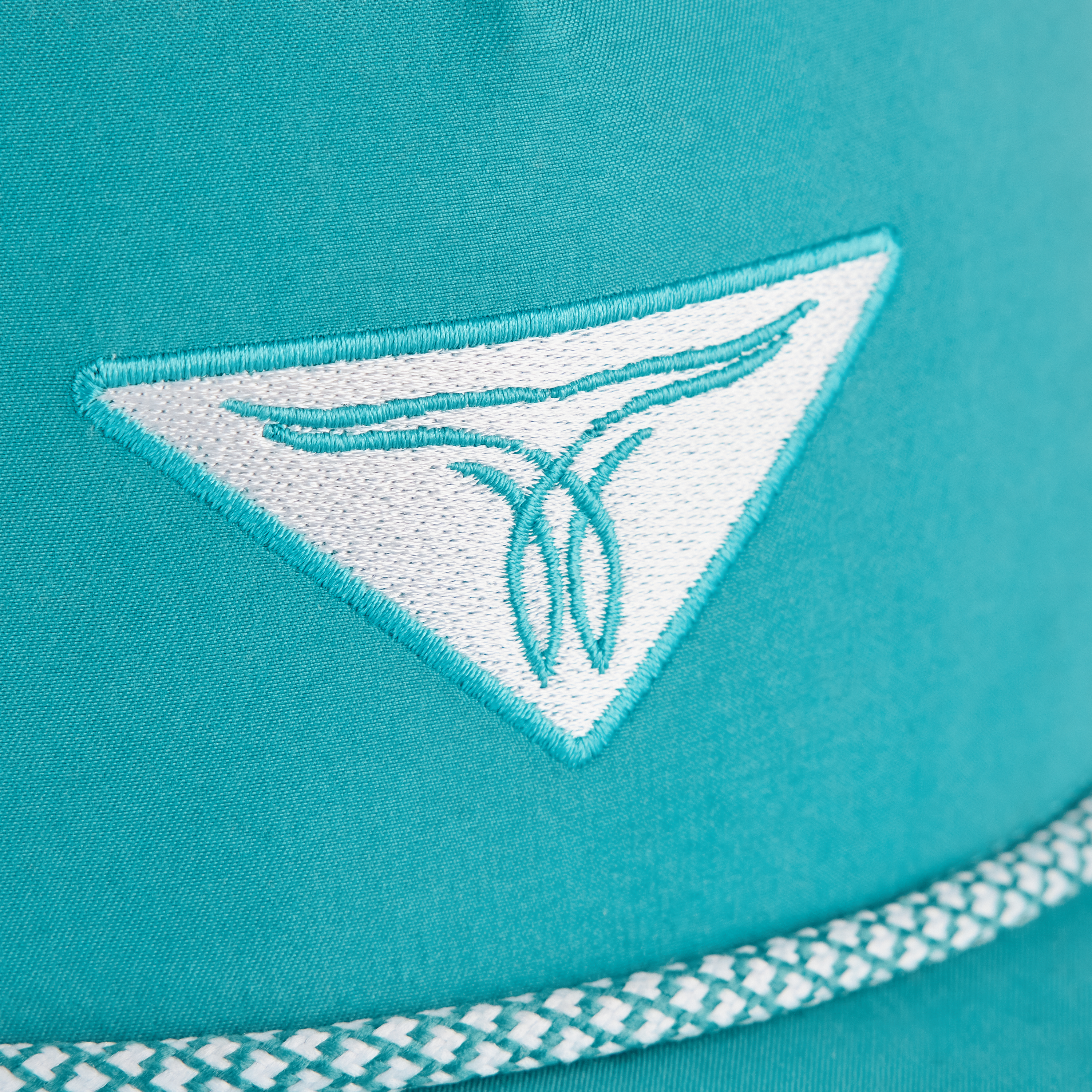 A close-up of a turquoise hat with a white and turquoise embroidered triangular logo and decorative trim along the edge