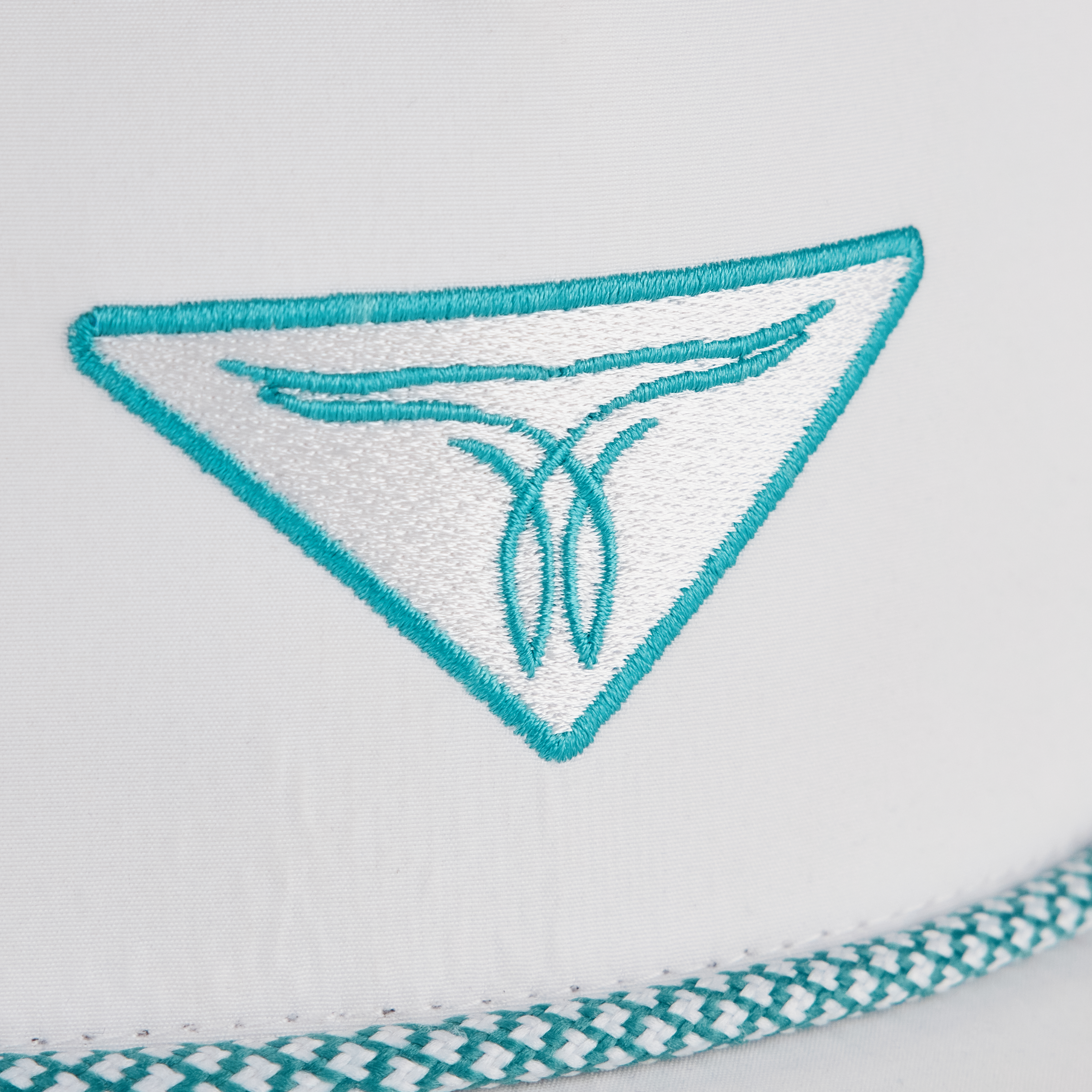 A close-up of a white hat with a turquoise embroidered triangular logo and decorative trim along the edge