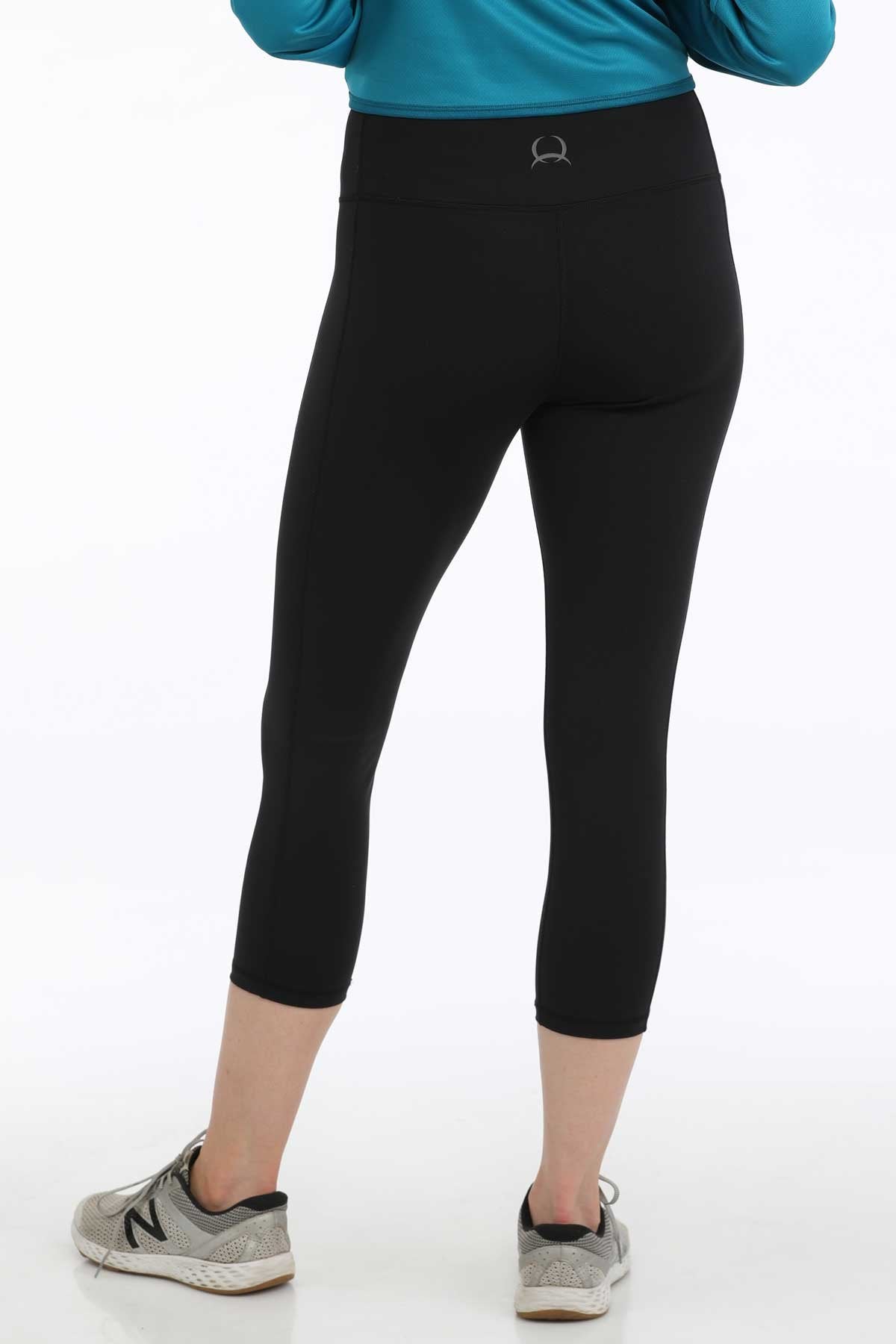 Back view of a woman wearing black cropped leggings with sneakers and a teal long-sleeve top displayed on a white background.