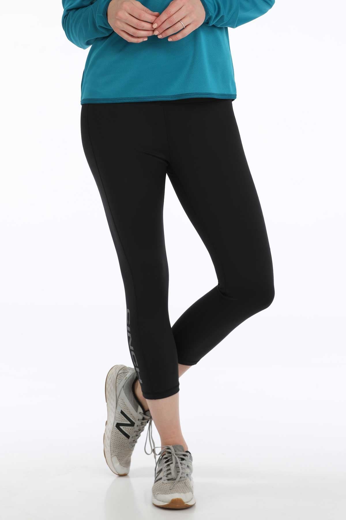Woman wearing black cropped leggings with sneakers and a teal long-sleeve top displayed on a white background.