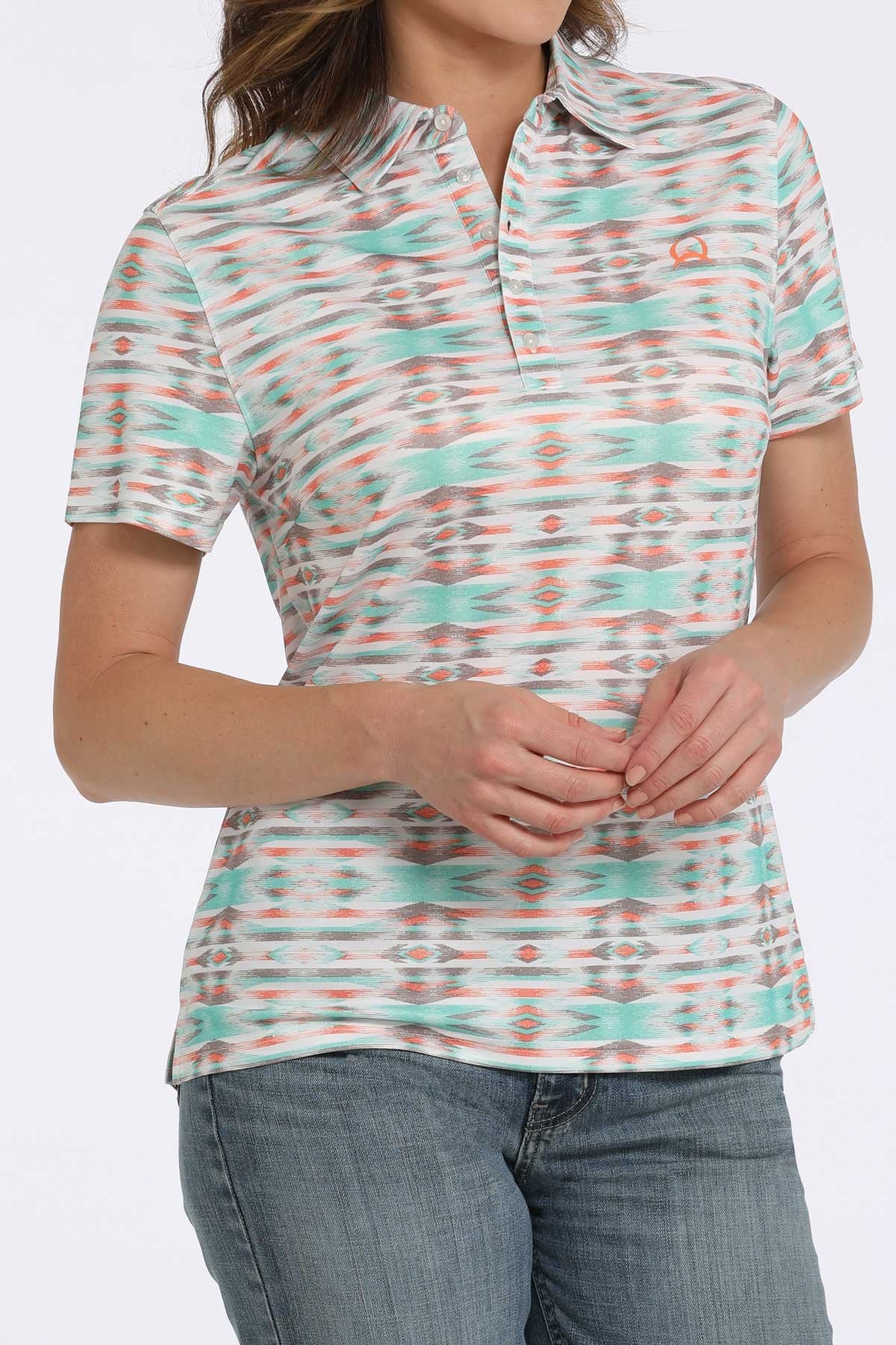 Woman wearing a short-sleeve collared shirt with a turquoise, orange, and white patterned design paired with blue jeans displayed on a white background.