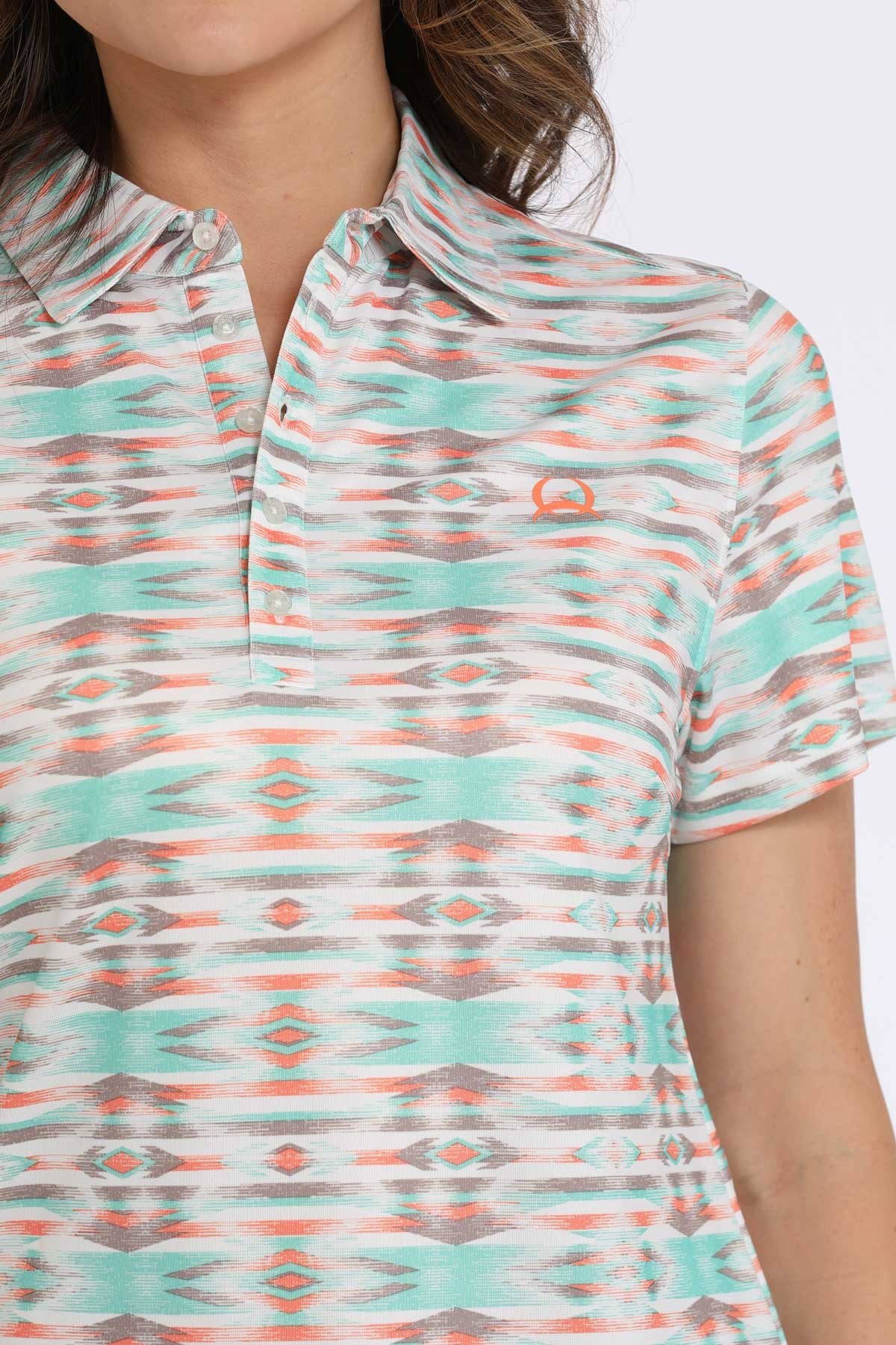 Close-up of a woman wearing a short-sleeve collared shirt with a turquoise, orange, and white patterned design displayed on a white background.