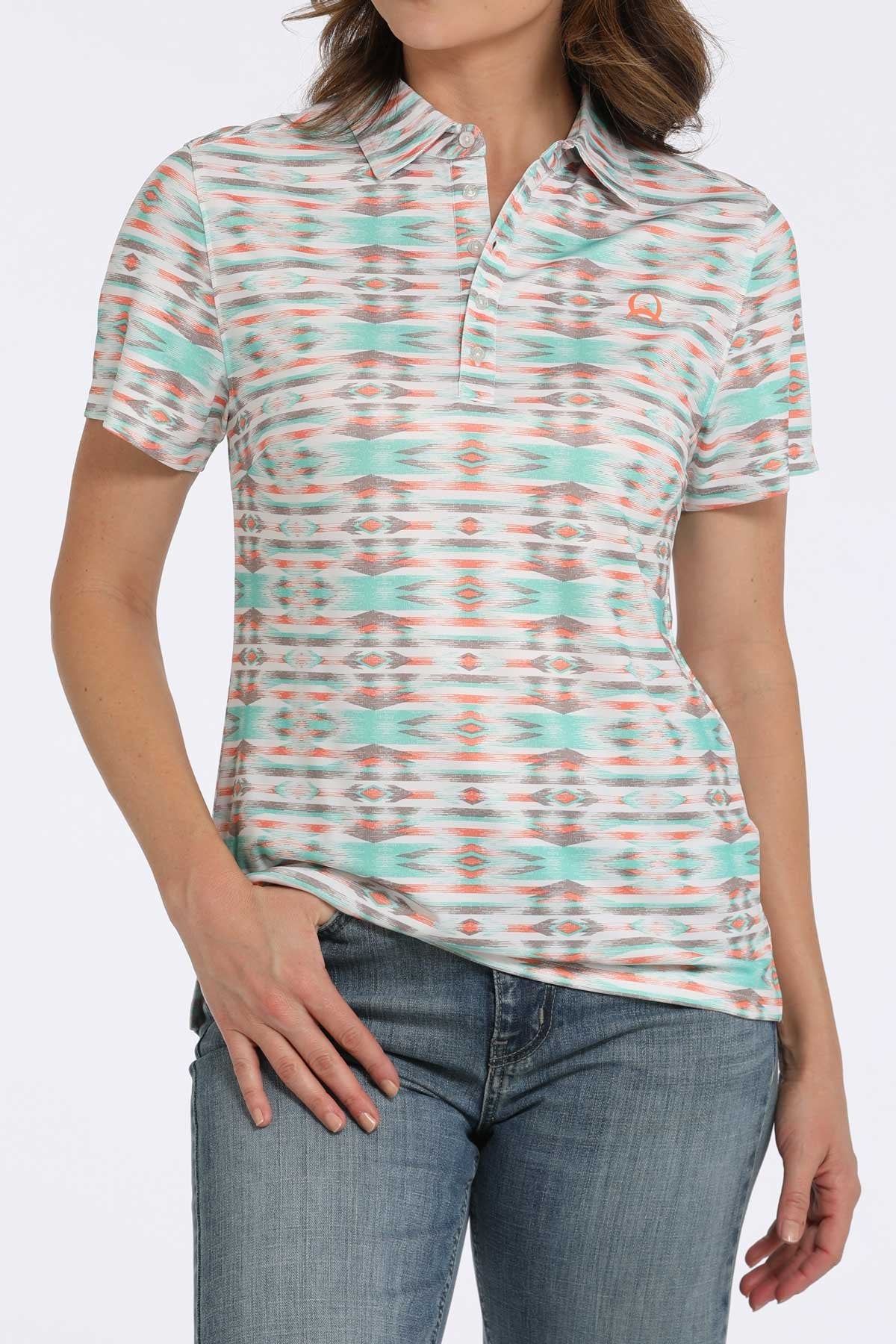 Woman wearing a short-sleeve collared shirt with a turquoise, orange, and white patterned design paired with blue jeans displayed on a white background.