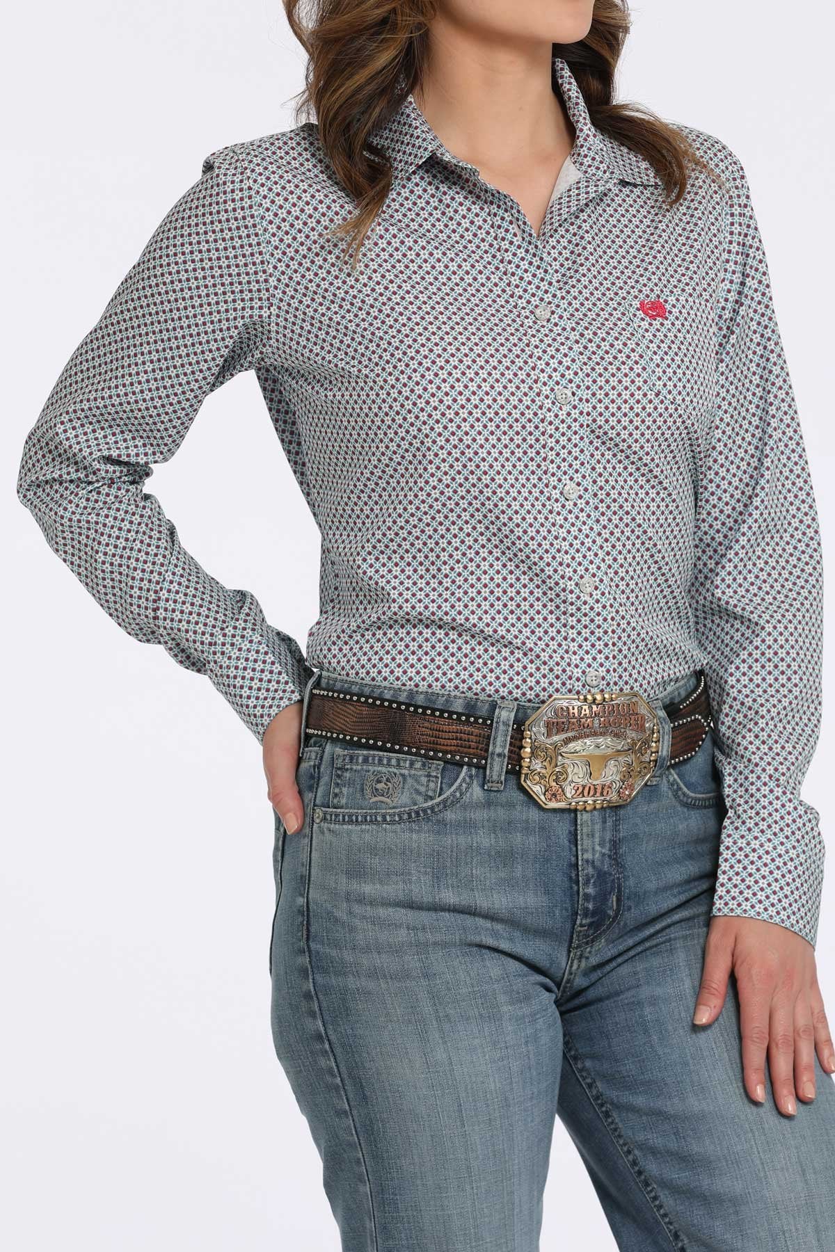 Woman wearing a gray button-down shirt with a small multicolor geometric pattern and a pink logo, paired with blue jeans and a western belt buckle displayed on a white background.