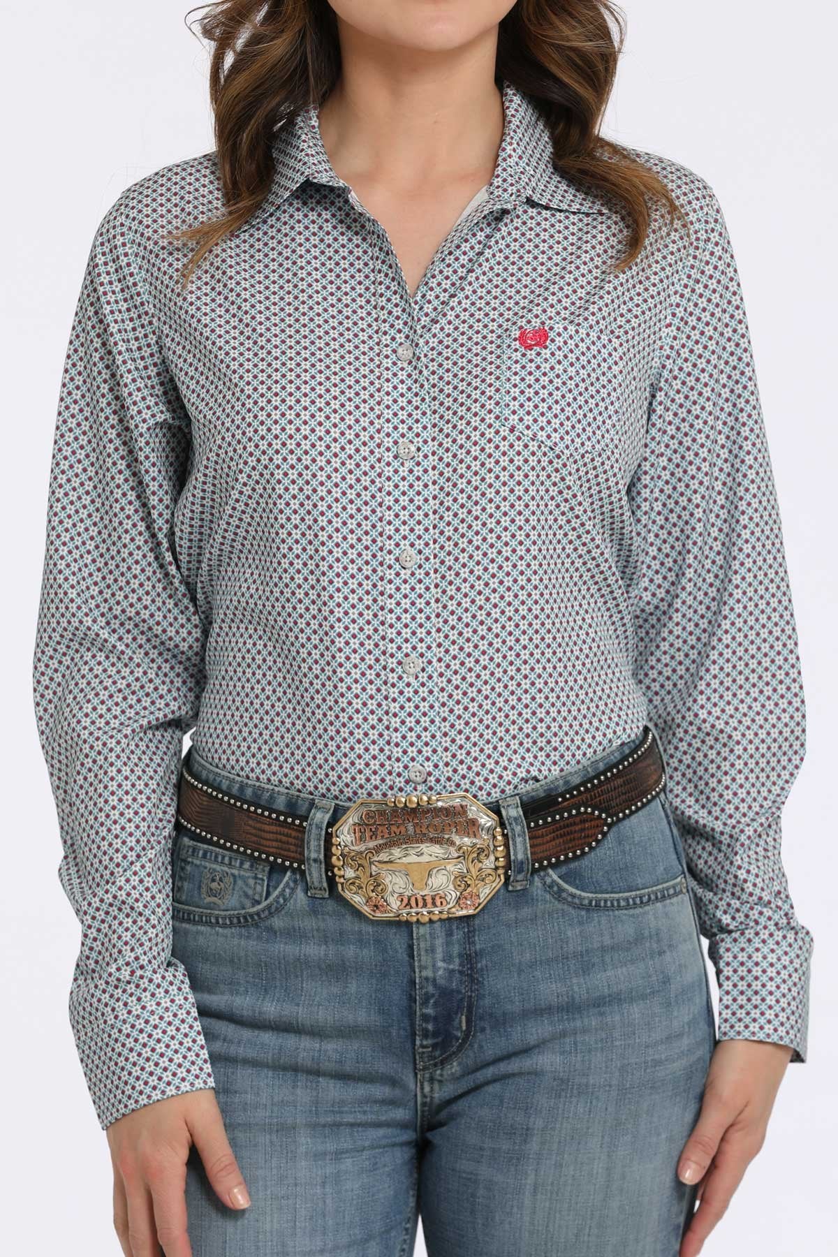 Woman wearing a gray button-down shirt with a small multicolor geometric pattern and a pink logo, paired with blue jeans and a western belt buckle displayed on a white background.