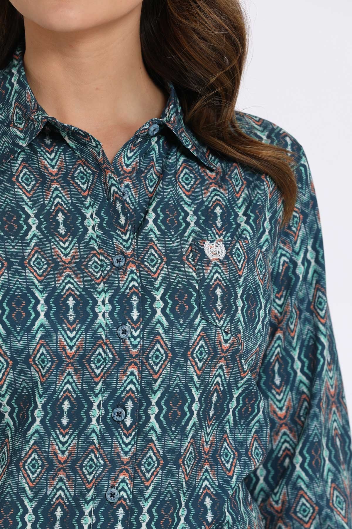 Close-up of a woman wearing a teal button-down shirt with a geometric diamond pattern displayed on a white background