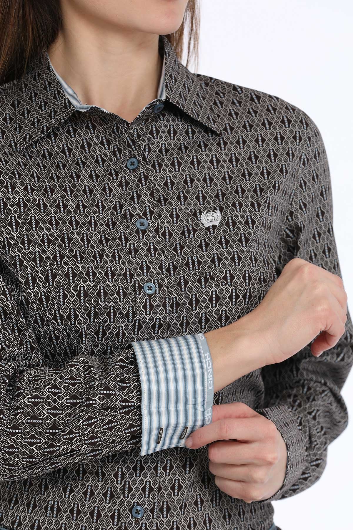 Close-up of a woman wearing a black button-down long sleeve western shirt with a geometric print and contrasting fabric inside the cuffs, displayed on a white background