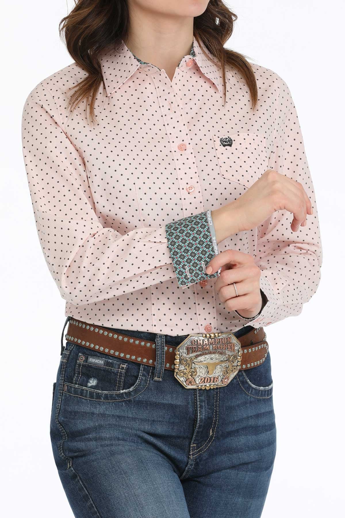 Woman wearing a pink patterned shirt and blue jeans with a belt and large buckle.