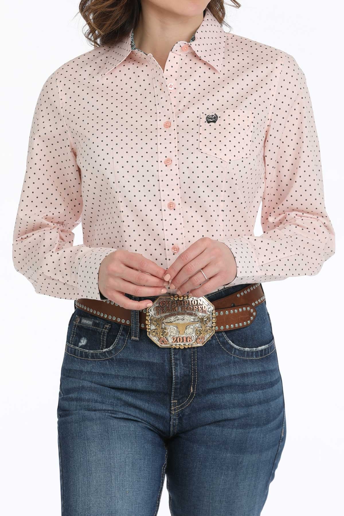 Person wearing a pink patterned shirt and blue jeans with a large belt buckle.