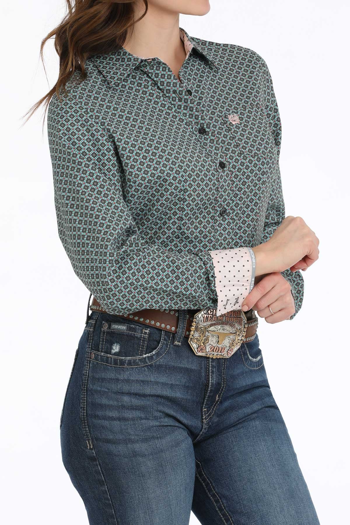 Person wearing a patterned long-sleeve shirt and jeans with a belt and large buckle.