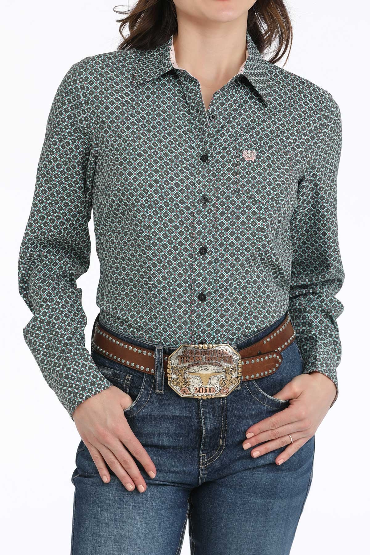 Woman wearing a patterned green shirt and jeans with a belt.