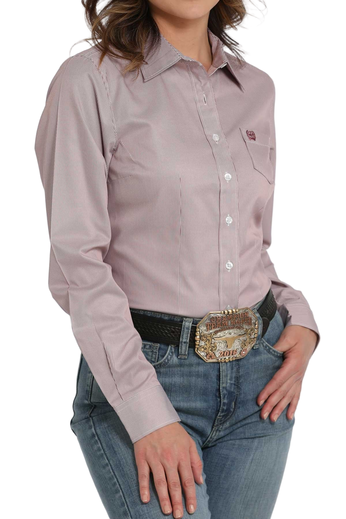 Woman wearing a pink striped long-sleeve button-down shirt, paired with jeans and a large western belt buckle