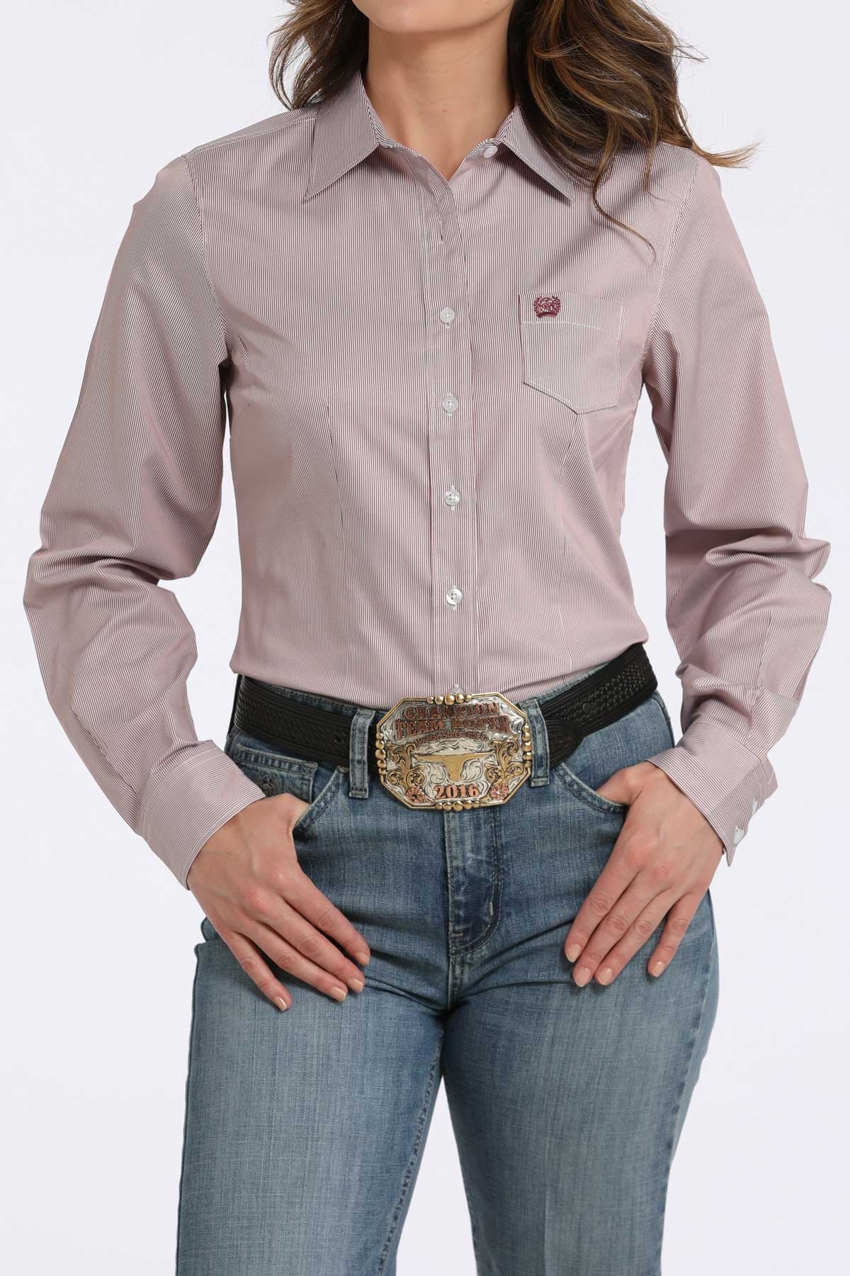 Woman wearing a light pink satin button-down shirt with a front pocket, paired with blue jeans and a western belt buckle displayed on a white background.