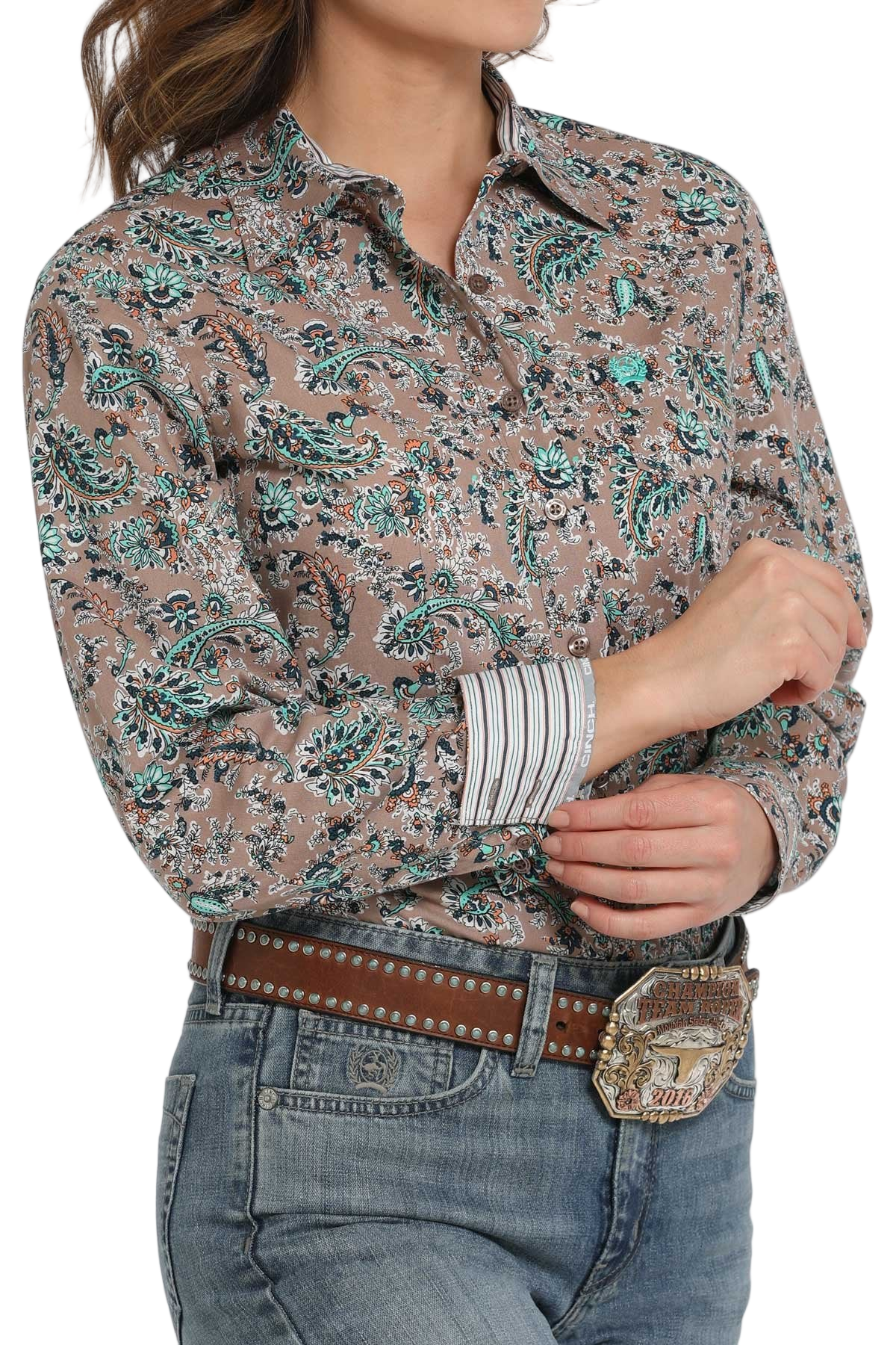 Woman wearing a patterned long-sleeve button-down shirt with contrasting cuffs, paired with jeans and a large western belt buckle