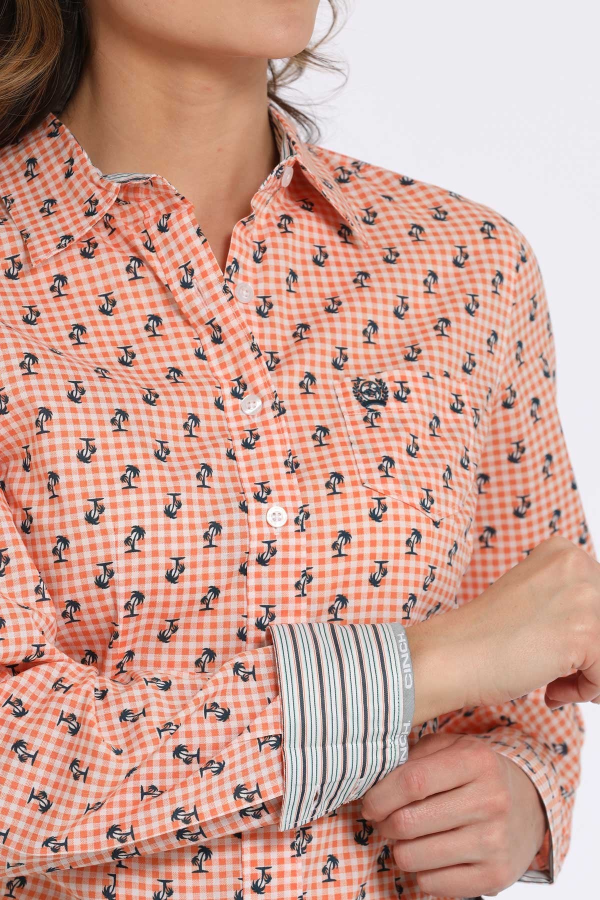 Close-up view of an orange checkered button-down shirt with a small navy floral pattern, showing contrasting striped fabric on the inside cuff displayed on a white background.
