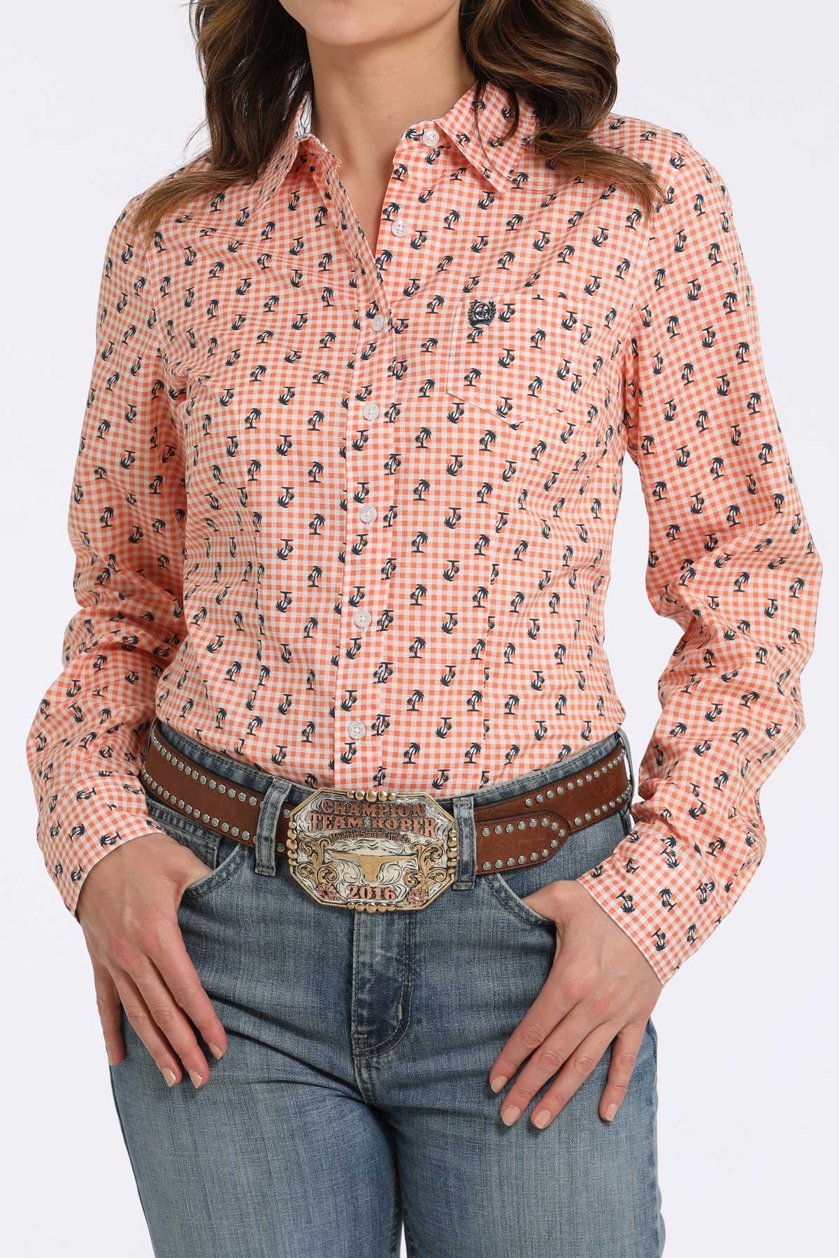 Woman wearing an orange checkered button-down shirt with a small navy floral pattern, paired with blue jeans and a western belt buckle displayed on a white background.