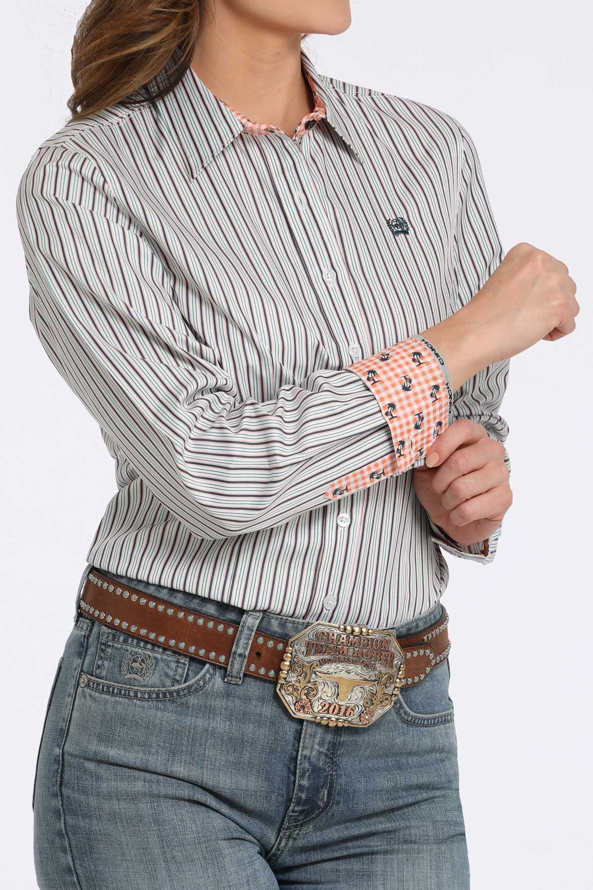 Woman wearing a white button-down shirt with black vertical stripes, showing contrasting orange patterned fabric on the inside collar and cuffs, paired with blue jeans displayed on a white background.