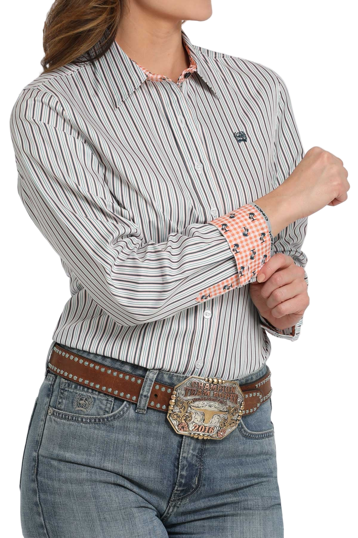 Woman wearing a light patterned long-sleeve button shirt with contrasting cuffs, paired with light-wash jeans and a brown belt with a large decorative buckle