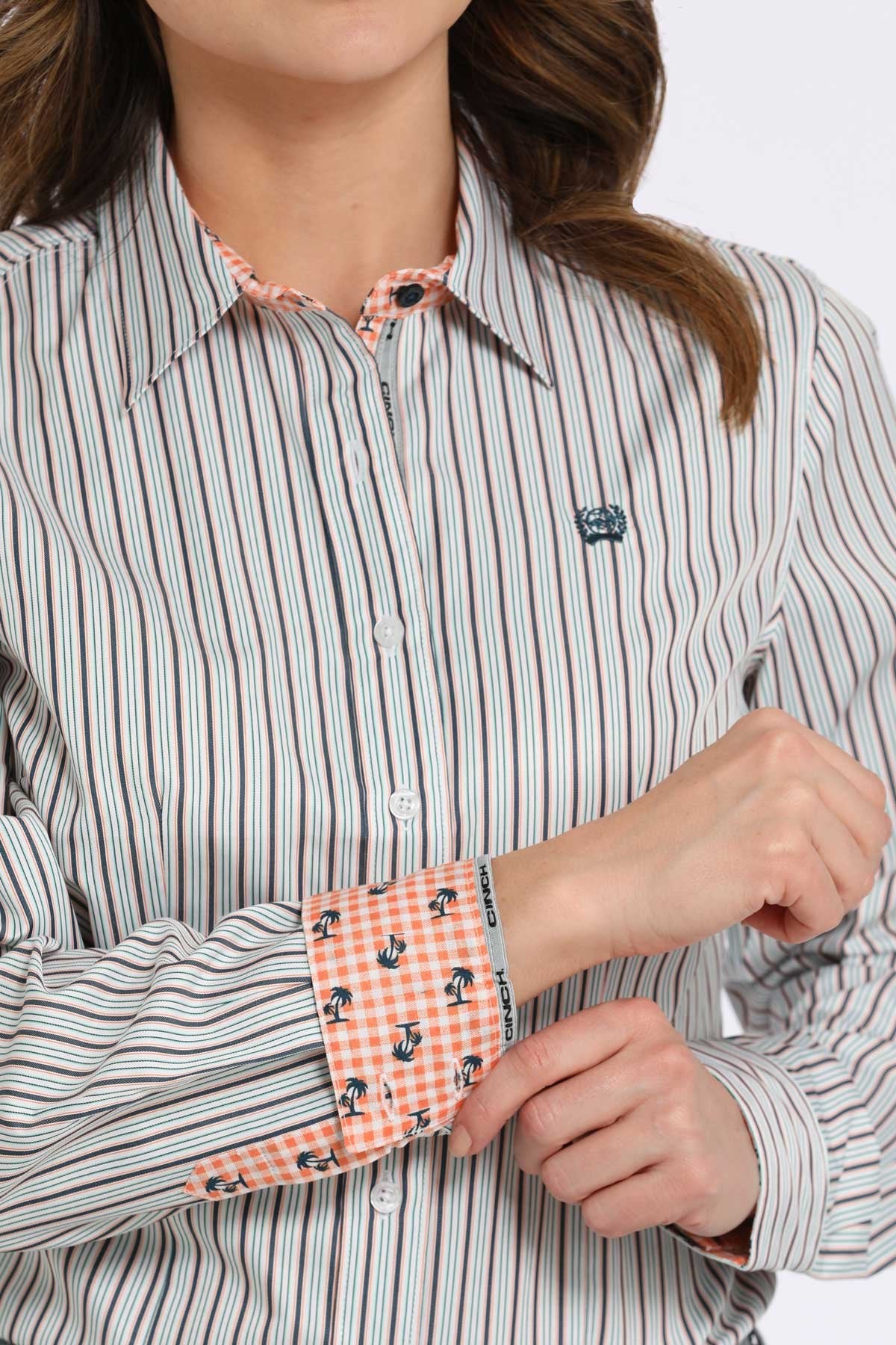 Close-up view of a woman wearing a white button-down shirt with black vertical stripes, showing contrasting orange patterned fabric on the inside collar and cuffs displayed on a white background.