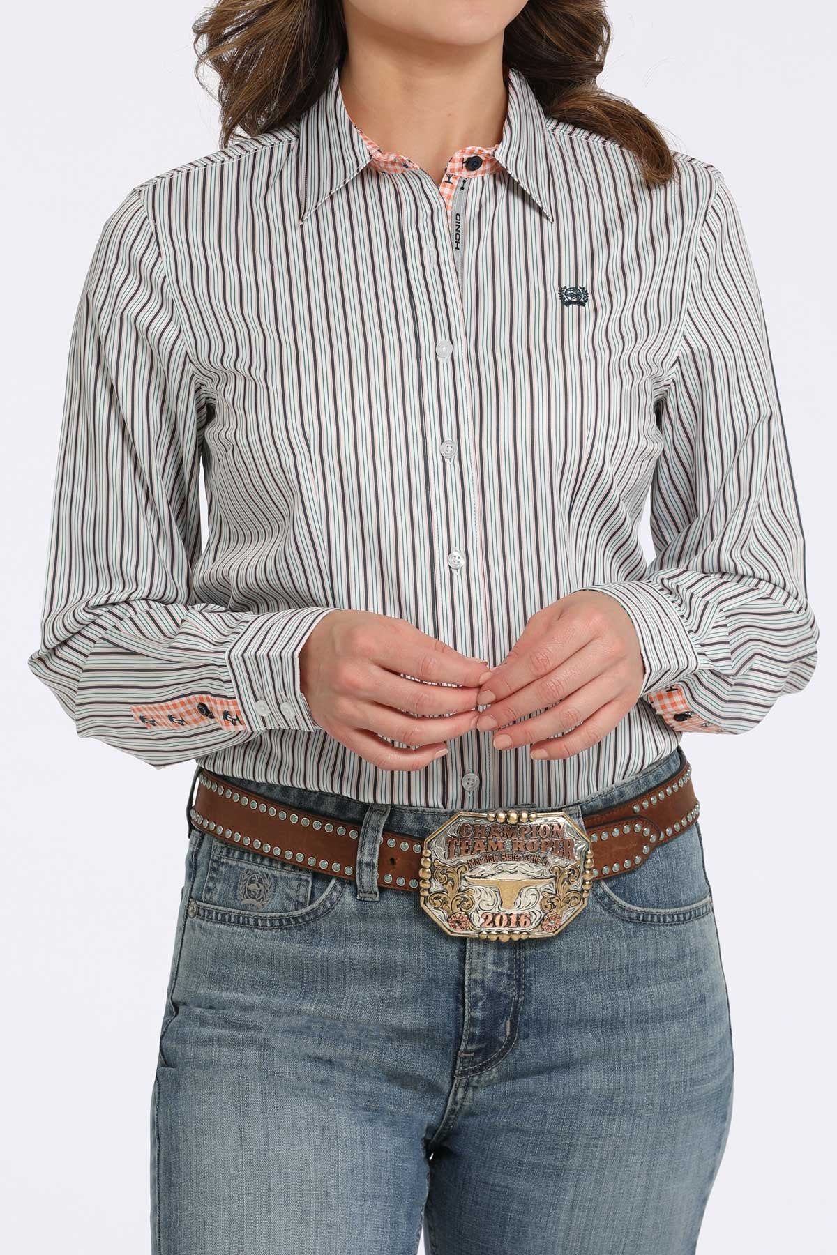 Woman wearing a white button-down shirt with black vertical stripes, paired with blue jeans and a western belt buckle displayed on a white background.