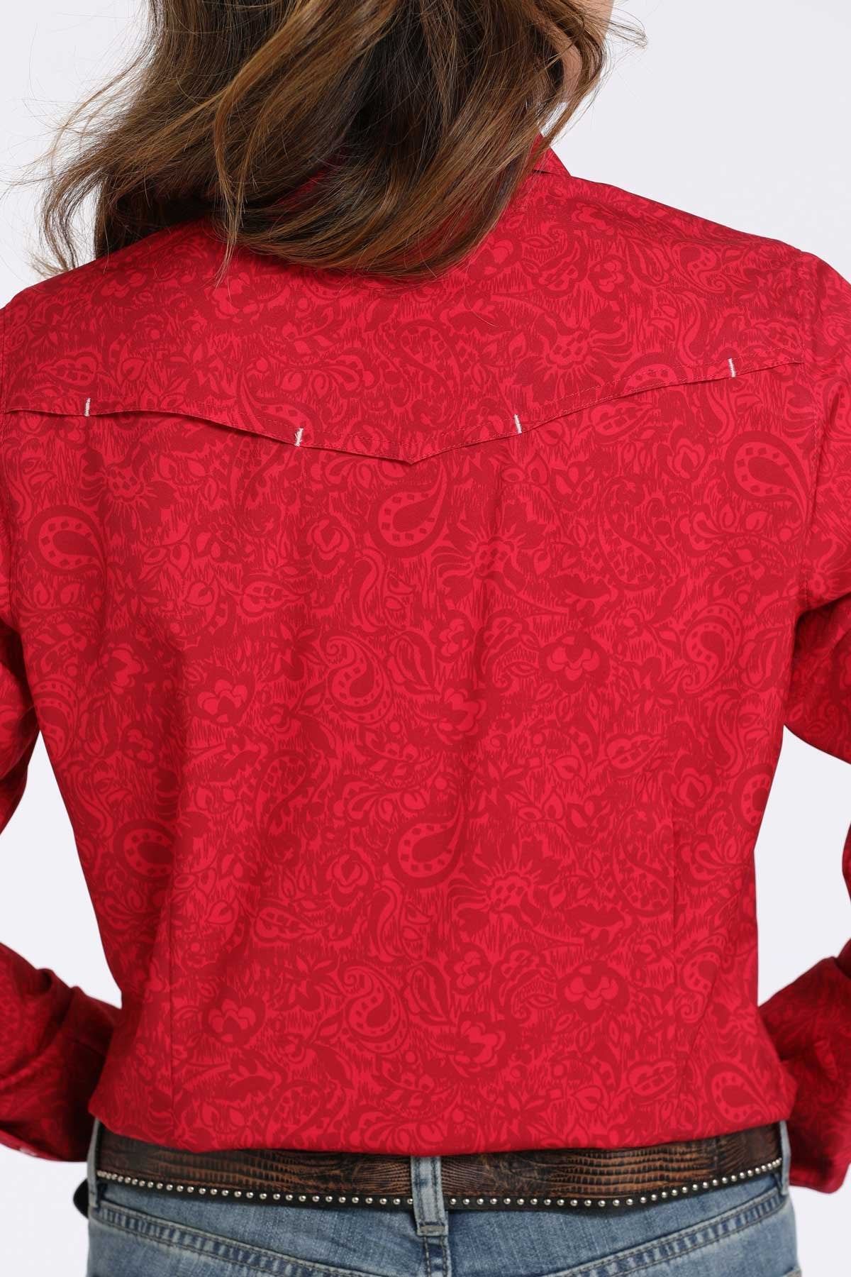 Back view of a woman wearing a pink long-sleeve shirt with subtle paisley pattern, paired with blue jeans displayed on a white background.