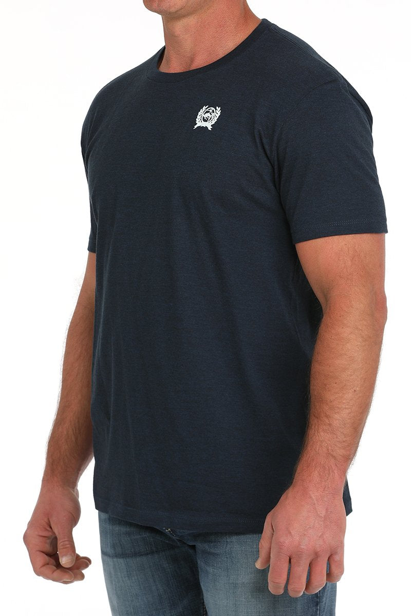Man wearing a dark navy short-sleeve t-shirt with a small white graphic on the chest and blue jeans displayed on a white background.