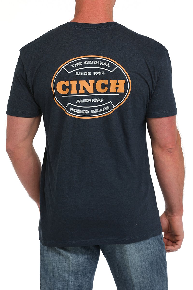 Back view of a man wearing a dark navy short-sleeve t-shirt with a large circular CINCH logo in orange and white, paired with blue jeans displayed on a white background.