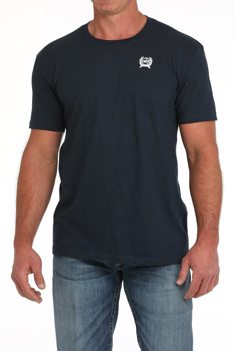Man wearing a dark navy short-sleeve t-shirt with a small white graphic on the chest and blue jeans displayed on a white background.