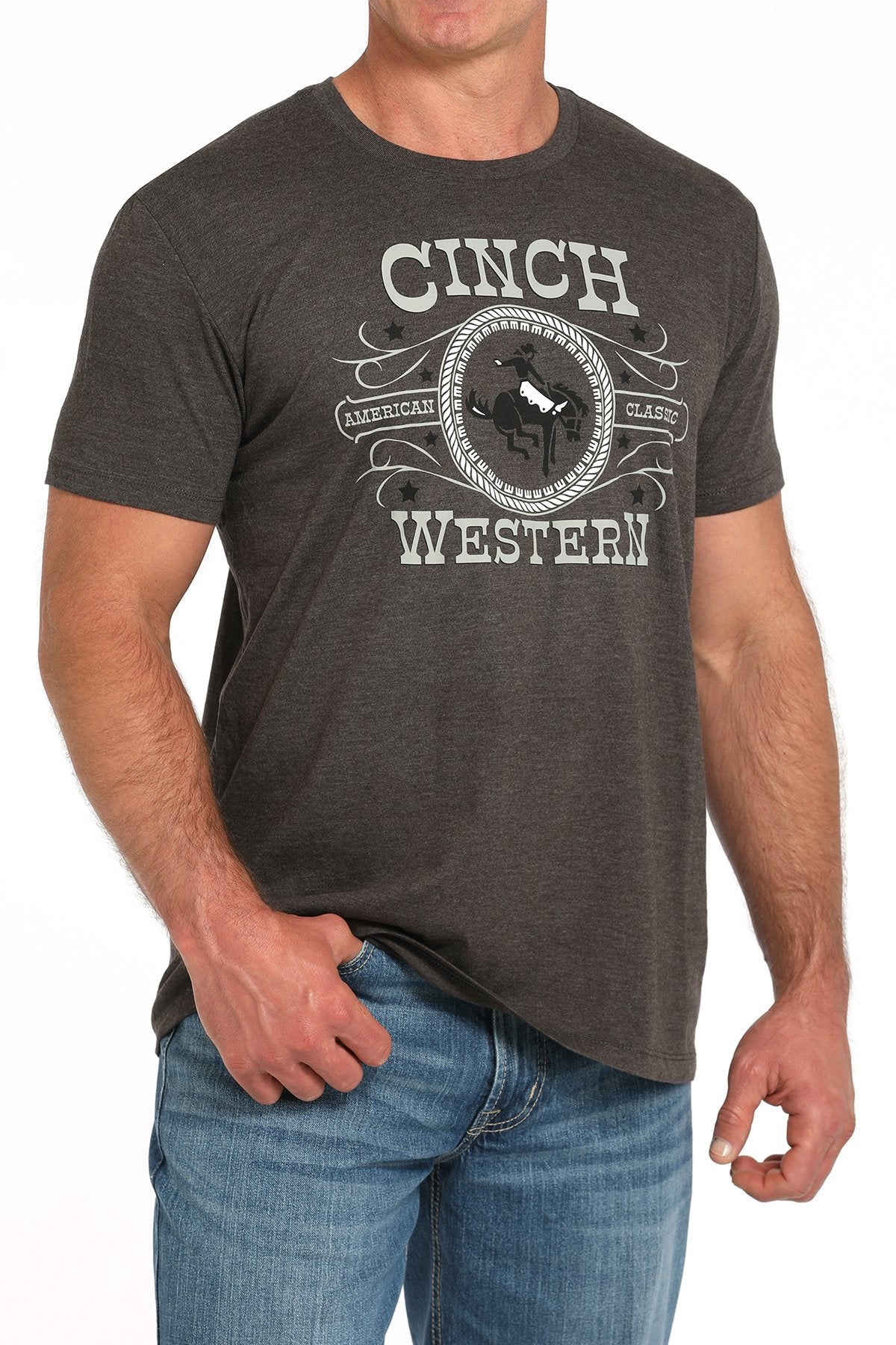 Side angled view of a man wearing a gray short-sleeve t-shirt with a large CINCH Western graphic, paired with blue jeans displayed on a white background.