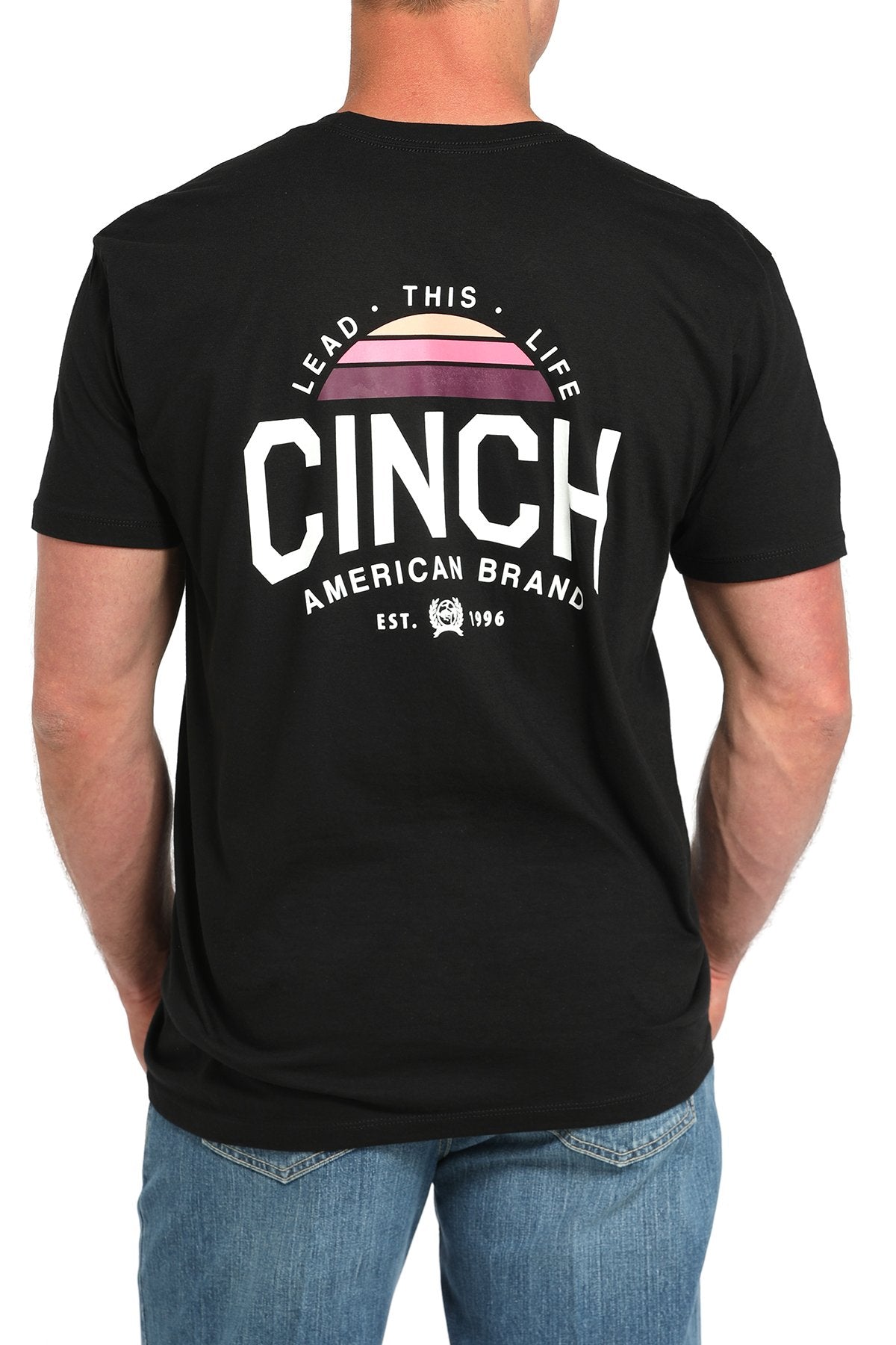 Back view of a man wearing a black short-sleeve t-shirt with a large CINCH graphic and colorful design, paired with blue jeans displayed on a white background.