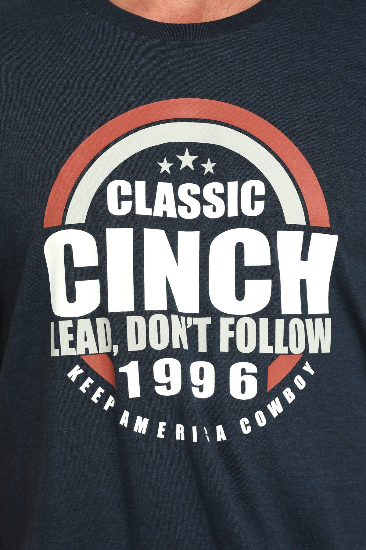 Close-up view of a navy blue short-sleeve t-shirt with a large circular CINCH graphic and 'Lead, Don’t Follow 1996' text displayed on a white background