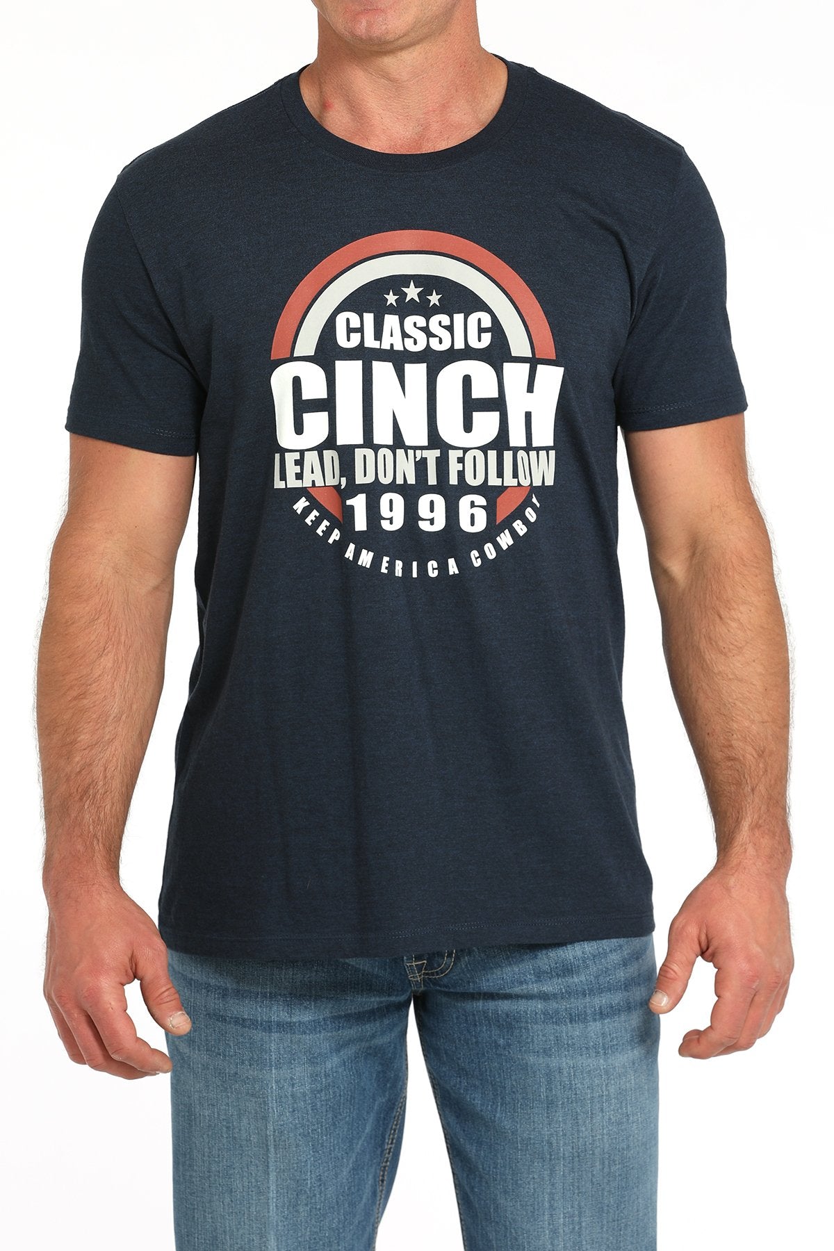 Front view of a man wearing a navy blue short-sleeve t-shirt with a large circular CINCH graphic and 'Lead, Don’t Follow 1996' text, paired with blue jeans displayed on a white background