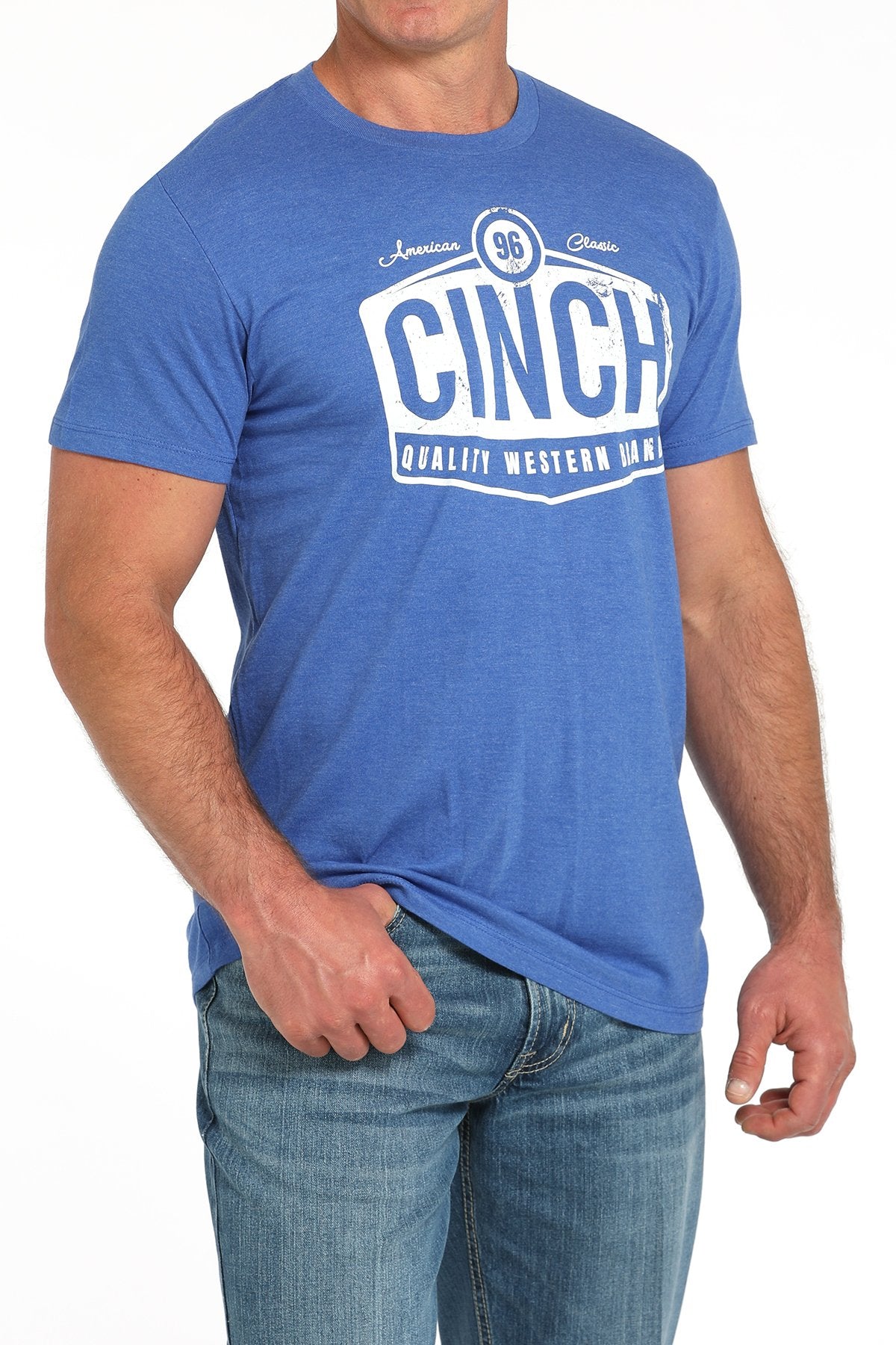 Side angled view of a man wearing a blue short-sleeve t-shirt with a large white CINCH graphic, paired with blue jeans displayed on a white background.