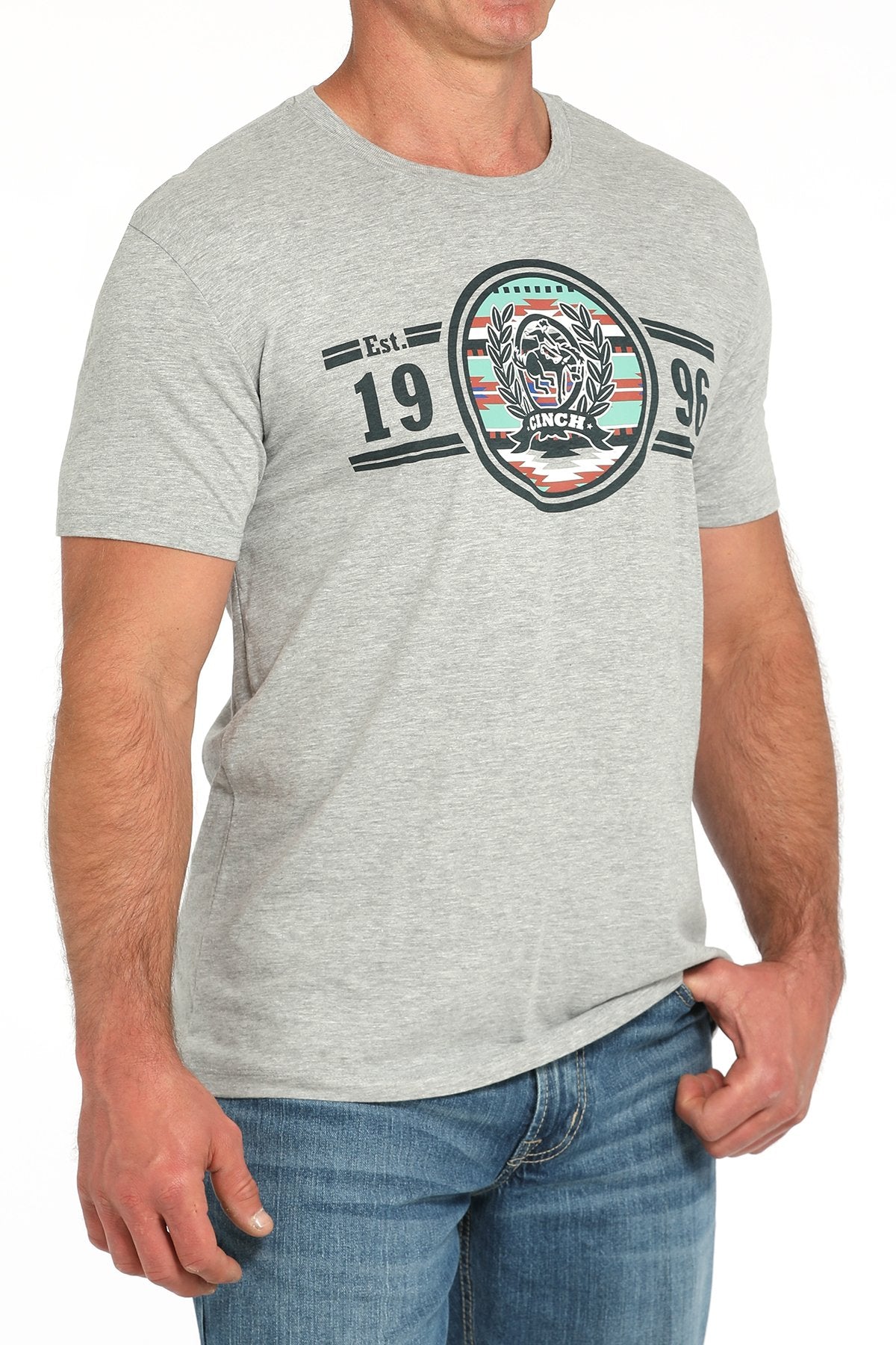 Side angled view of a man wearing a gray short-sleeve t-shirt with a circular CINCH graphic and '1996' text, paired with blue jeans displayed on a white background.