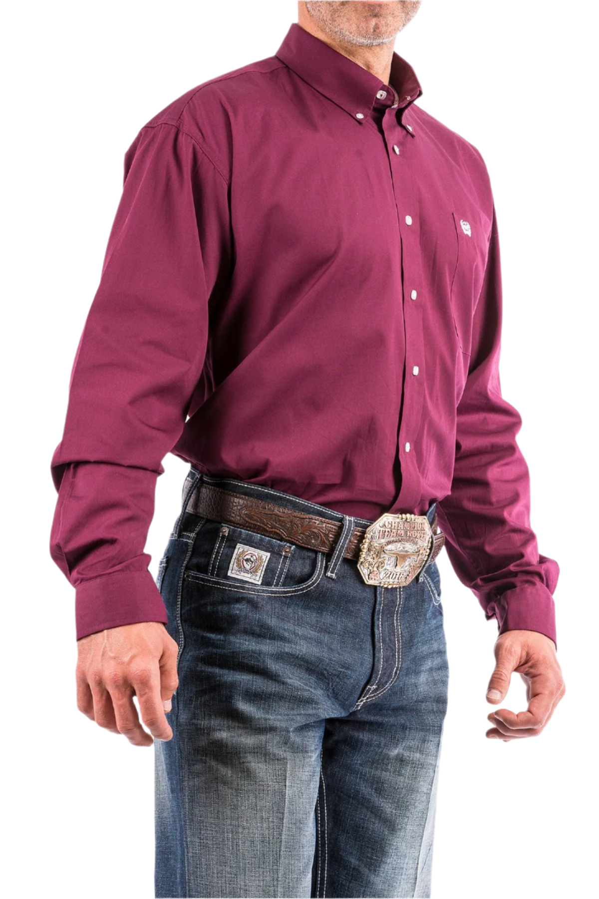 A man wearing a long sleeve burgundy solid color button-down shirt and blue jeans, with a belt and buckle visible.
