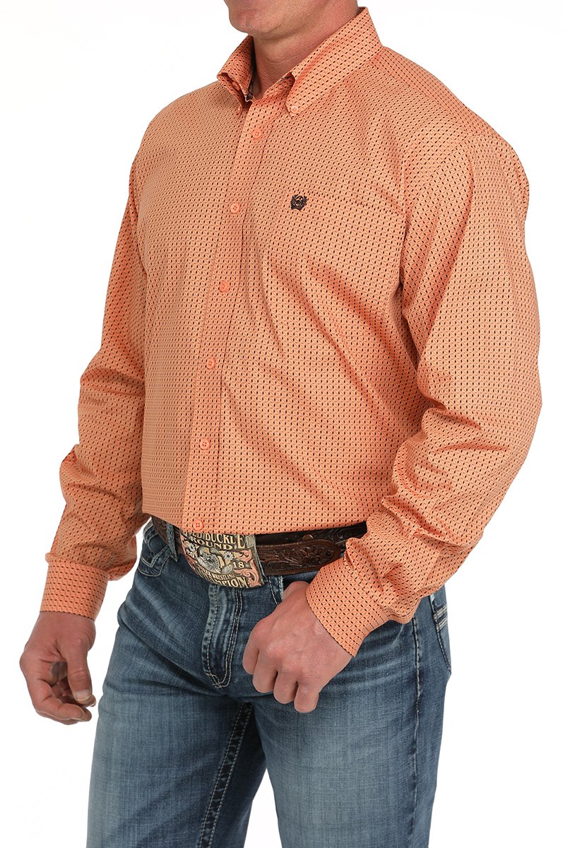Man wearing an orange button-down long sleeve western shirt with a small geometric print, paired with blue jeans and a leather belt with a large buckle. The shirt has a button-down collar and chest logo, displayed on a white background
