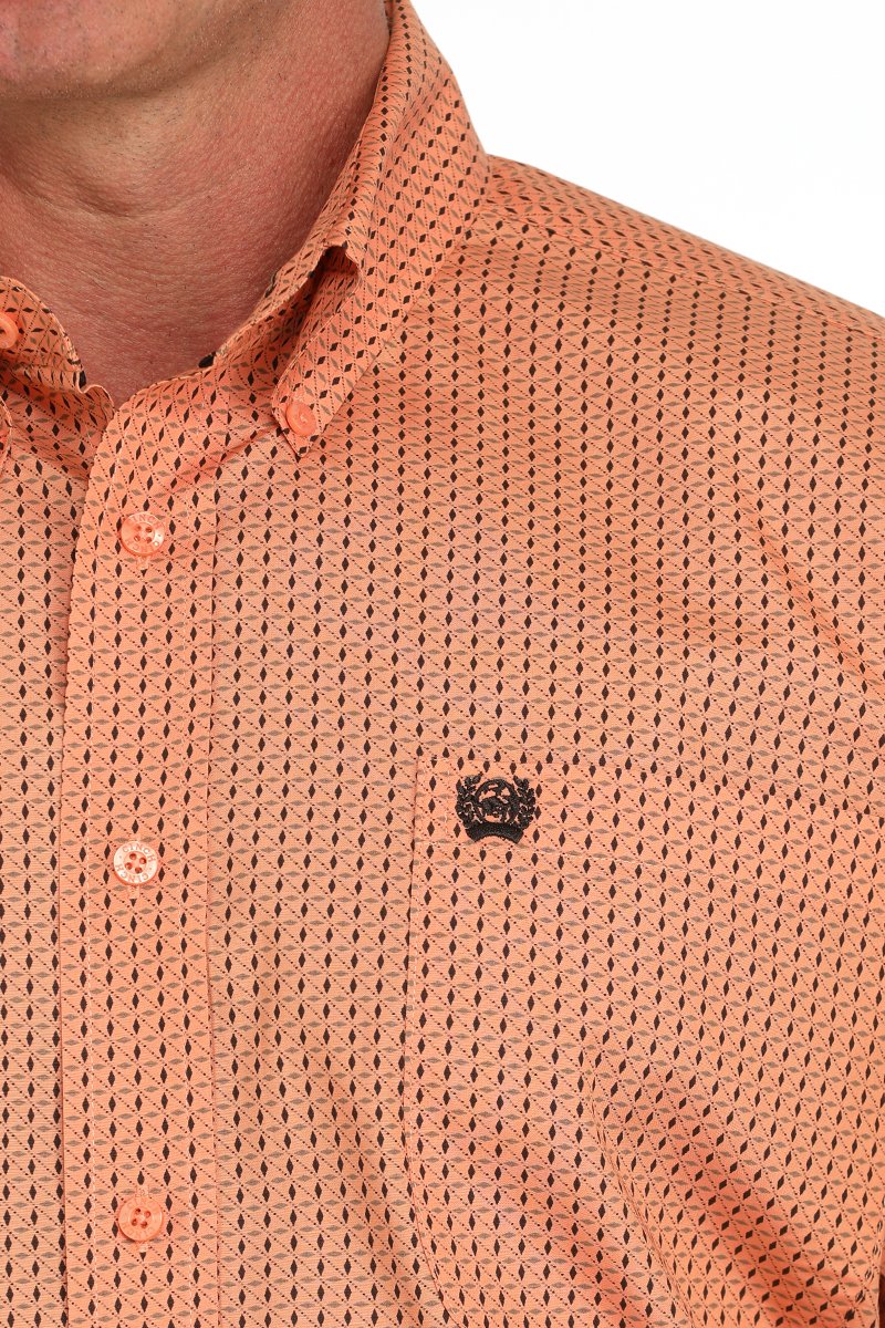 Close-up of a man wearing an orange button-down long sleeve western shirt with a small geometric print. The shirt has a button-down collar and chest logo, displayed on a white background