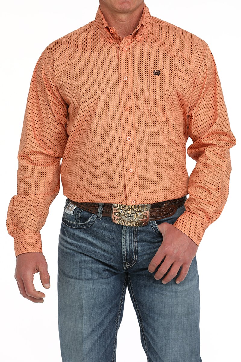 Man wearing an orange button-down long sleeve western shirt with a small geometric print, paired with blue jeans and a leather belt with a large buckle. The shirt has a button-down collar and chest logo, displayed on a white background