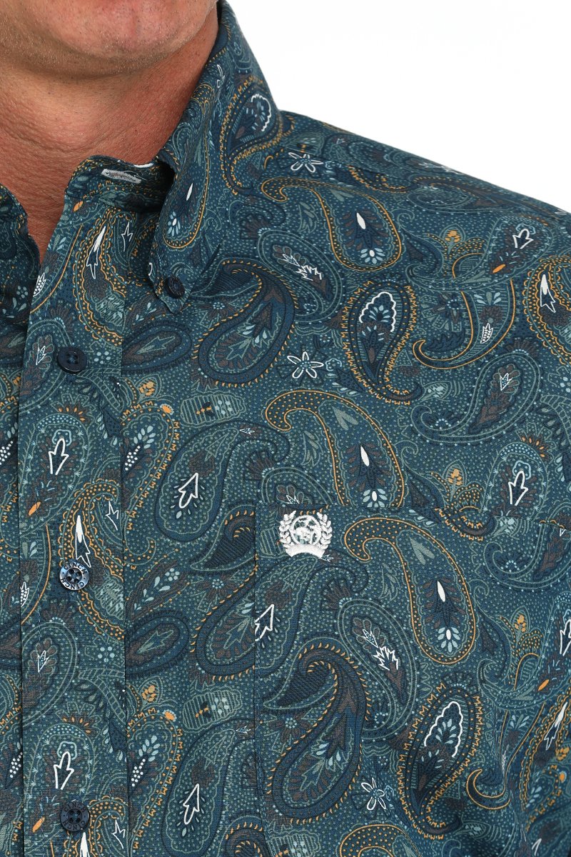 Close-up of a man wearing a dark teal paisley patterned button-down shirt displayed on a white background.