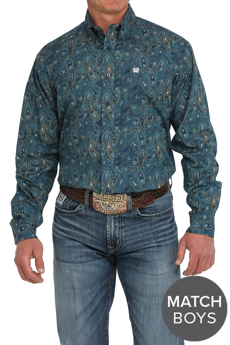 Man wearing a dark teal paisley patterned button-down shirt tucked into blue jeans with a western belt buckle displayed on a white background.