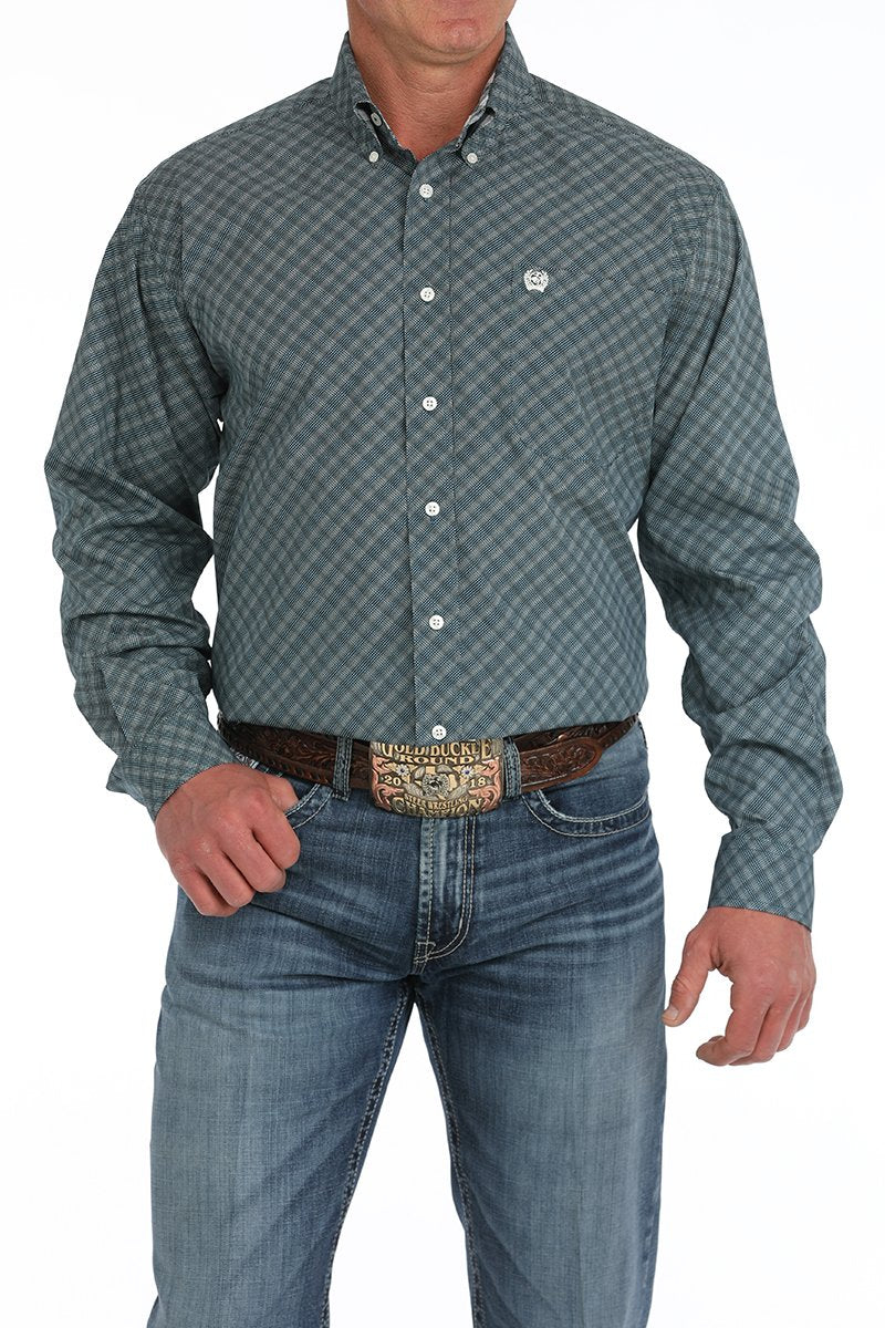 Man wearing a teal patterned button-down shirt tucked into blue jeans with a western belt buckle displayed on a white background.