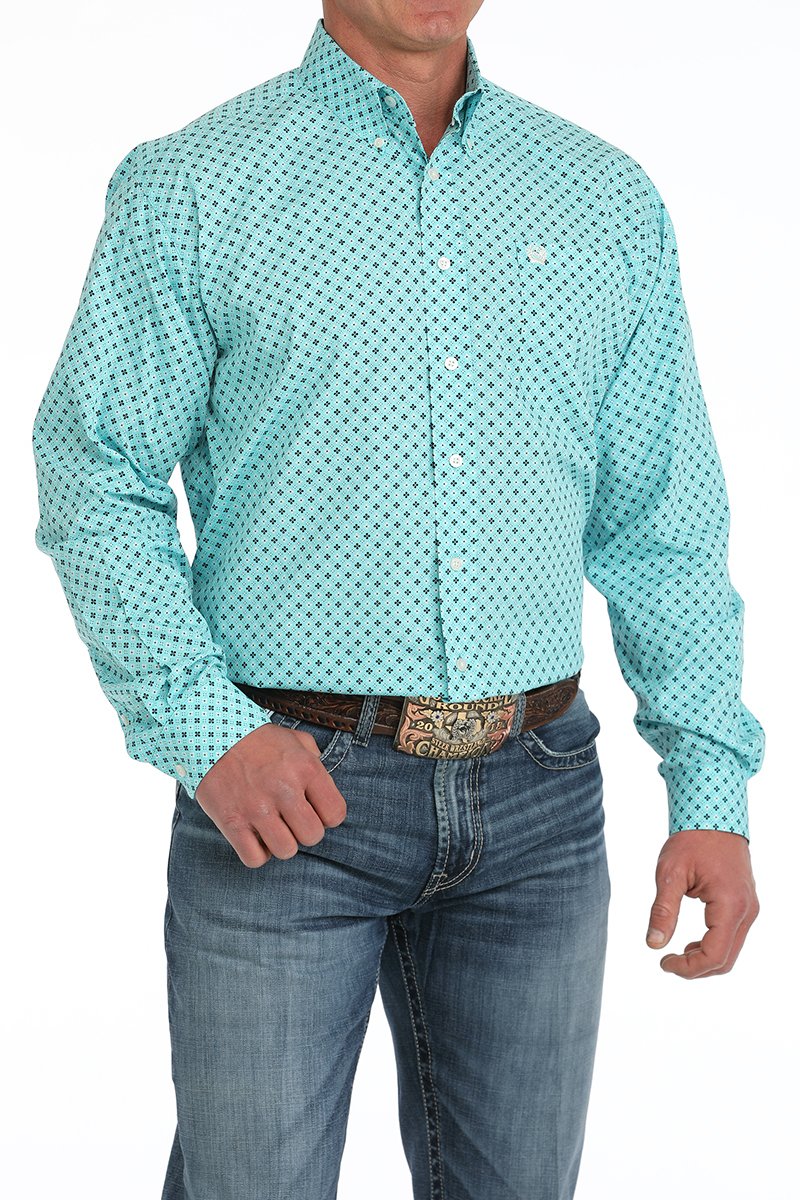 Man wearing a turquoise patterned button-down shirt tucked into blue jeans with a western belt buckle displayed on a white background.