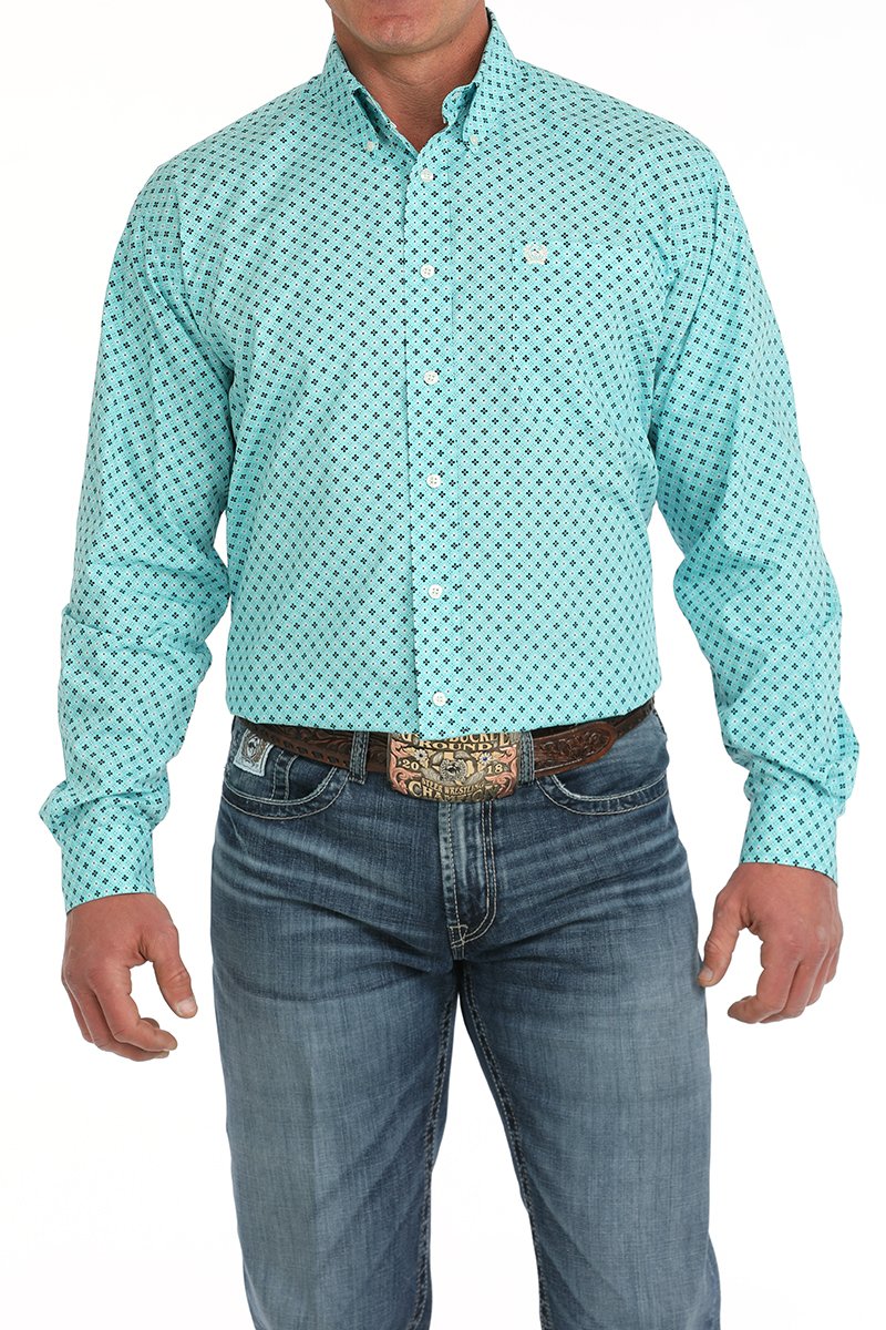 Man wearing a turquoise patterned button-down shirt tucked into blue jeans with a western belt buckle displayed on a white background.