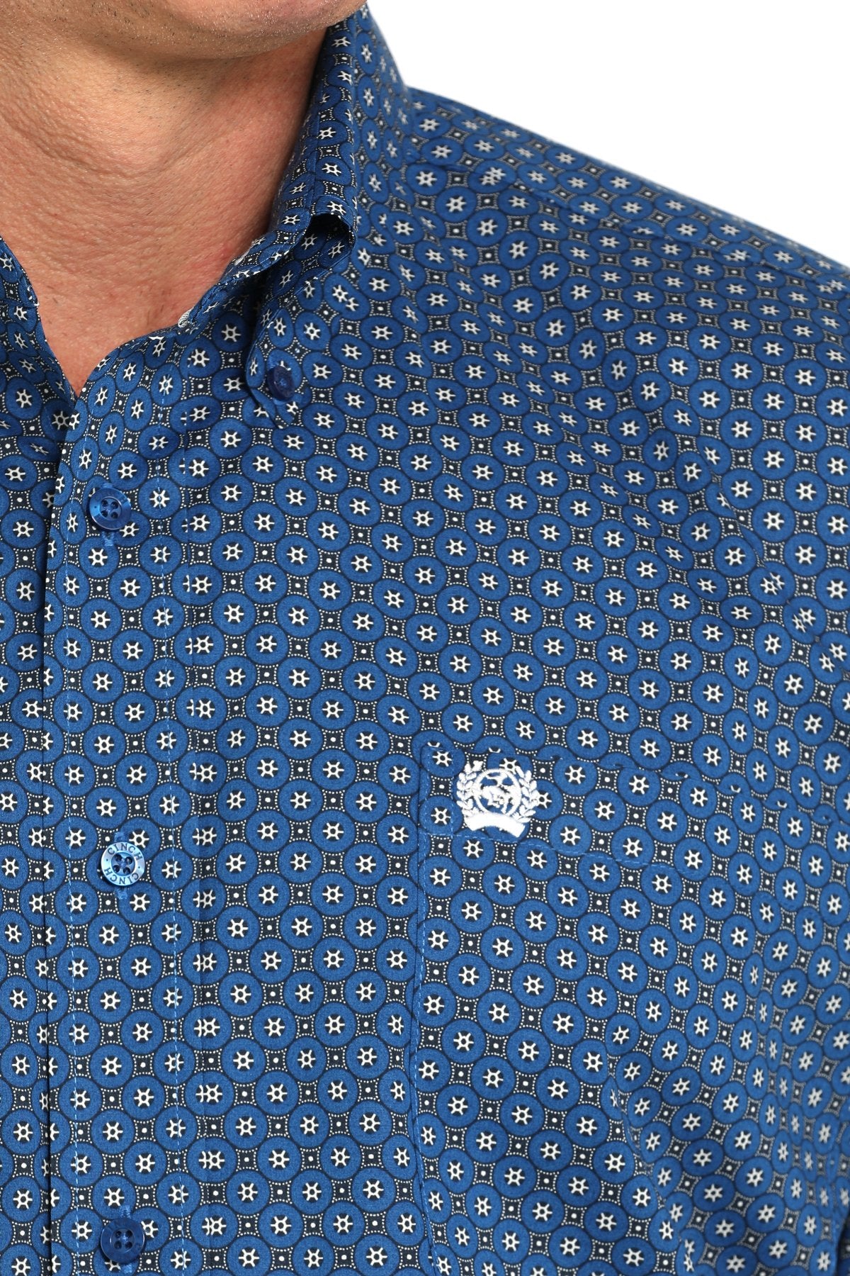 Close-up view of a royal blue long-sleeve button-down shirt with a small geometric print pattern and chest logo displayed on a white background.