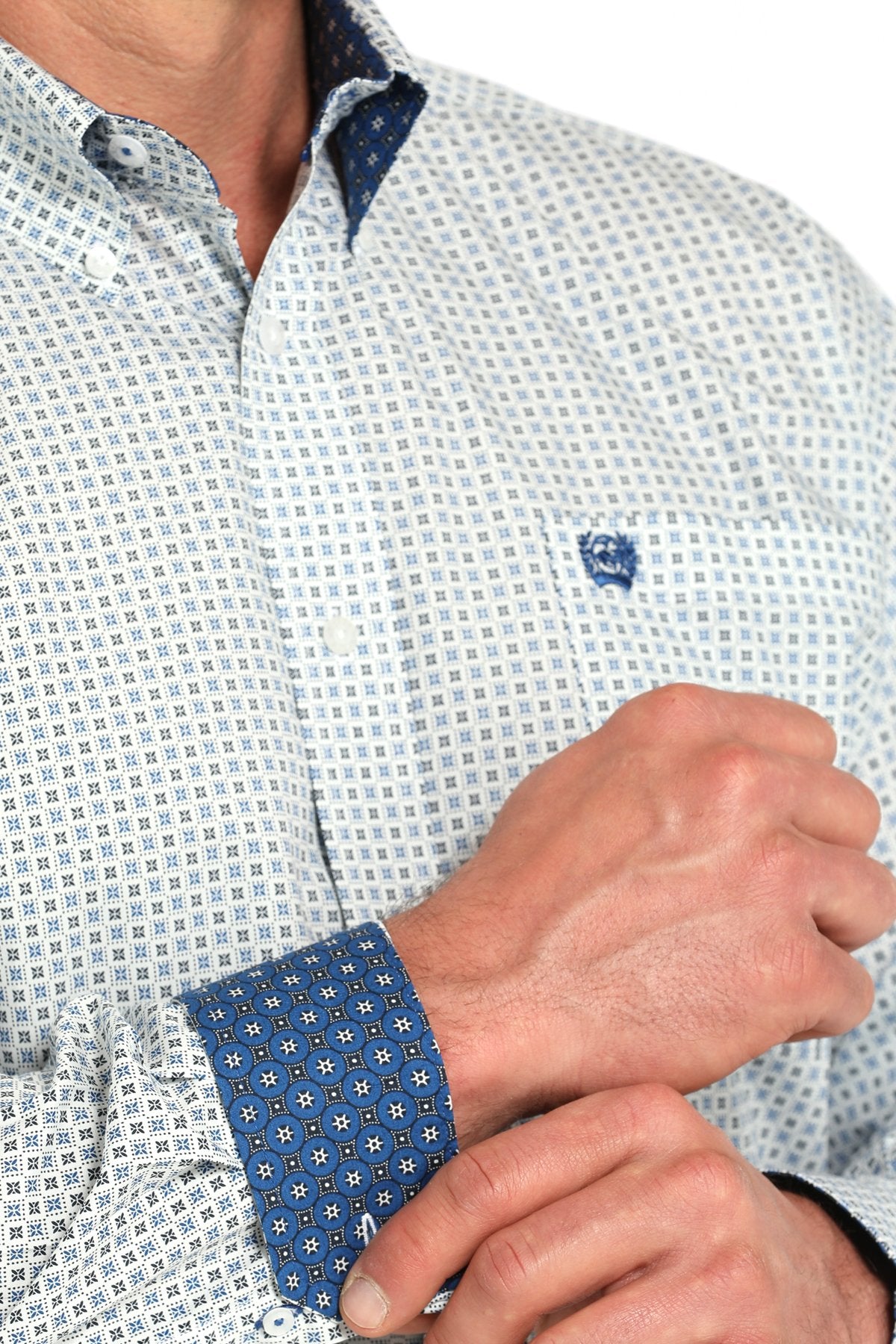 Close-up view of a white long-sleeve button-down shirt with a blue geometric print pattern and contrasting cuff detail displayed on a white background.