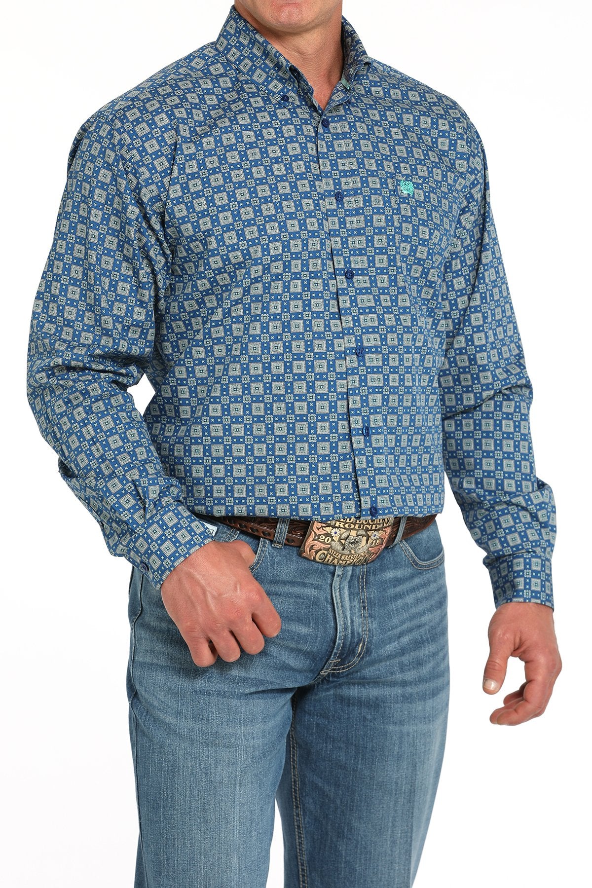 Side angled view of a man wearing a royal blue long-sleeve button-down shirt with a medallion print pattern, paired with blue jeans and a western belt buckle displayed on a white background.