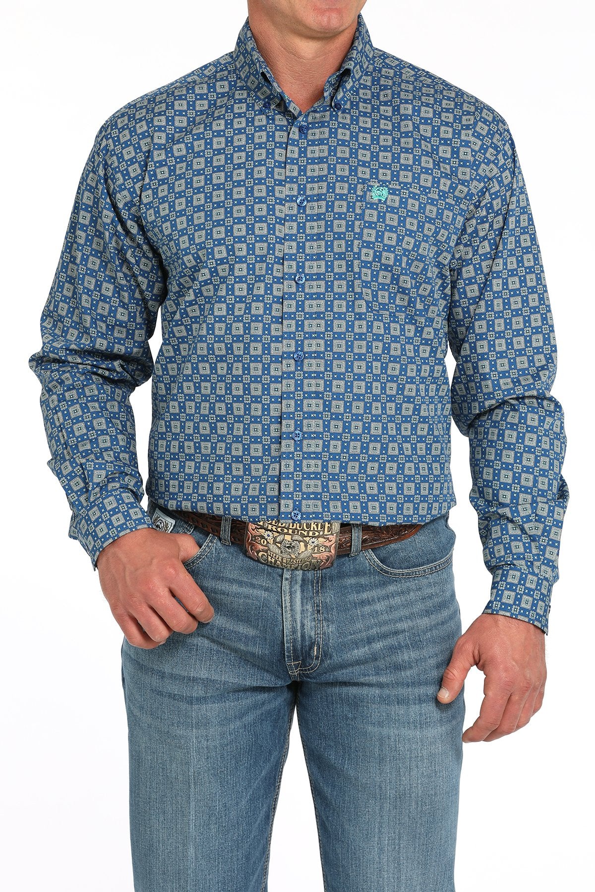 Front view of a man wearing a royal blue long-sleeve button-down shirt with a medallion print pattern, paired with blue jeans and a western belt buckle displayed on a white background.